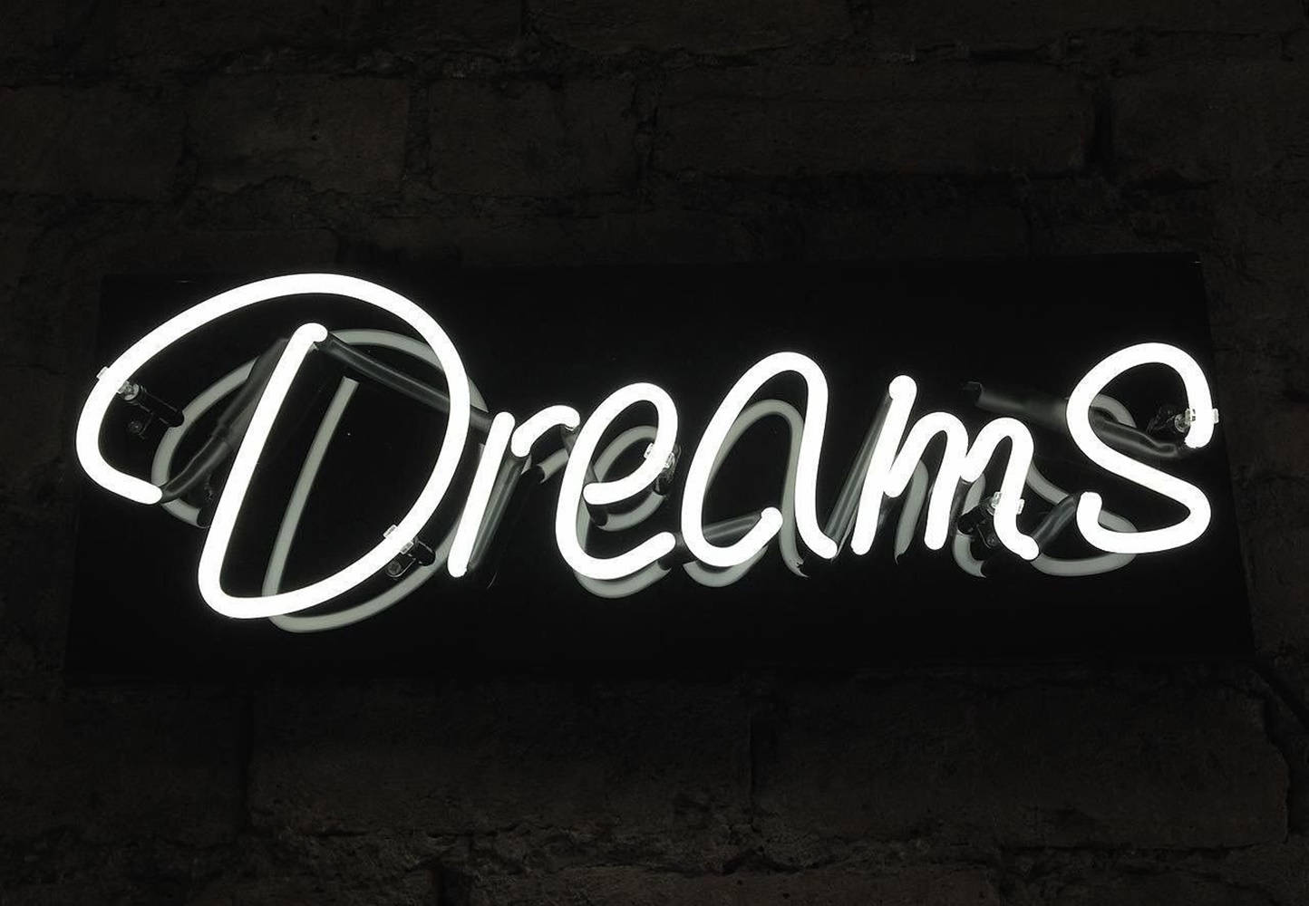 一個發光的白色霓虹燈牌，上面寫著 'Dreams'，安裝在深色磚牆上。 — Juice Wrld 壁紙