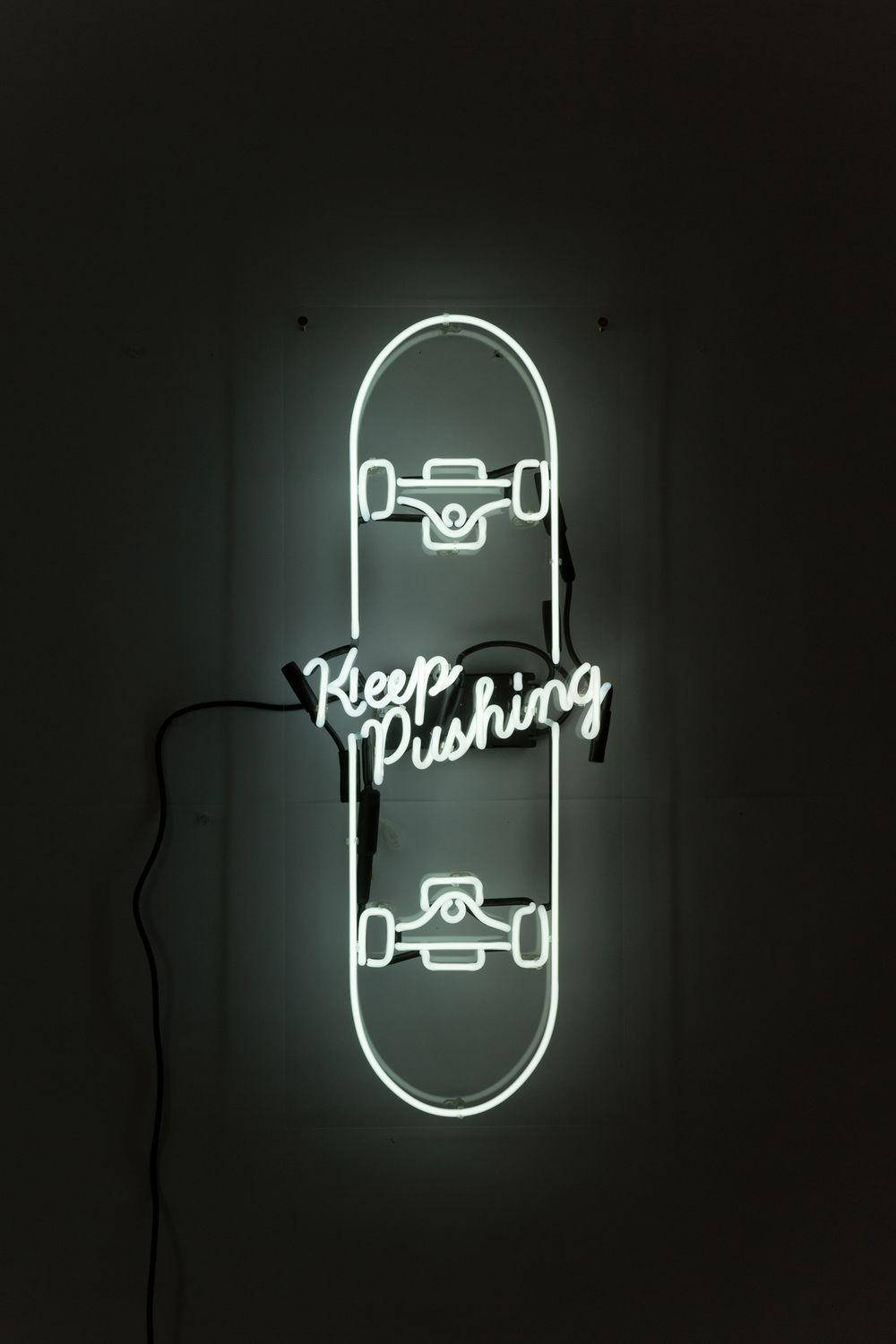 滑板 桌布 壁紙 — 一個發光的白色霓虹燈牌，形狀像滑板，上面有「Keep Pushing」的字樣，在黑暗的牆壁上亮起。