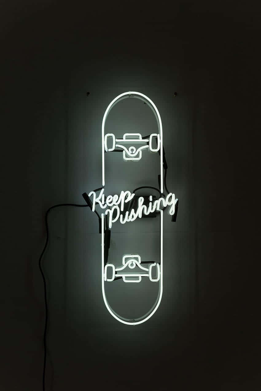 Skater Girl Aesthetic 桌布 壁紙 — 一個發光的白色霓虹燈牌，形狀像滑板，上面寫著「Keep Pushing」，照亮了黑暗的牆壁。