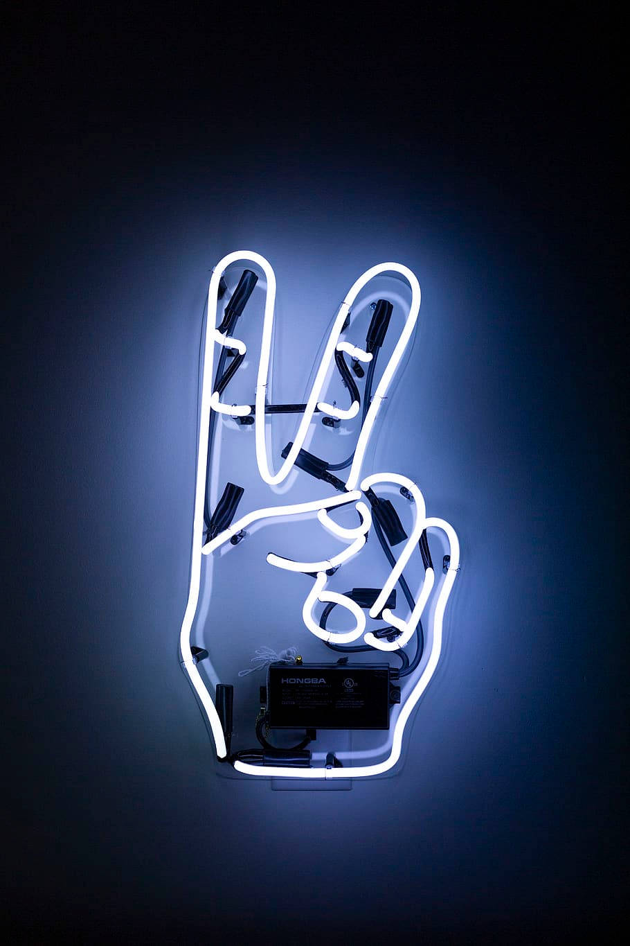 Peace Symbol 桌布 壁紙 — 一個發光的白色霓虹燈牌，形狀為和平手勢，安裝在深藍色牆壁上。