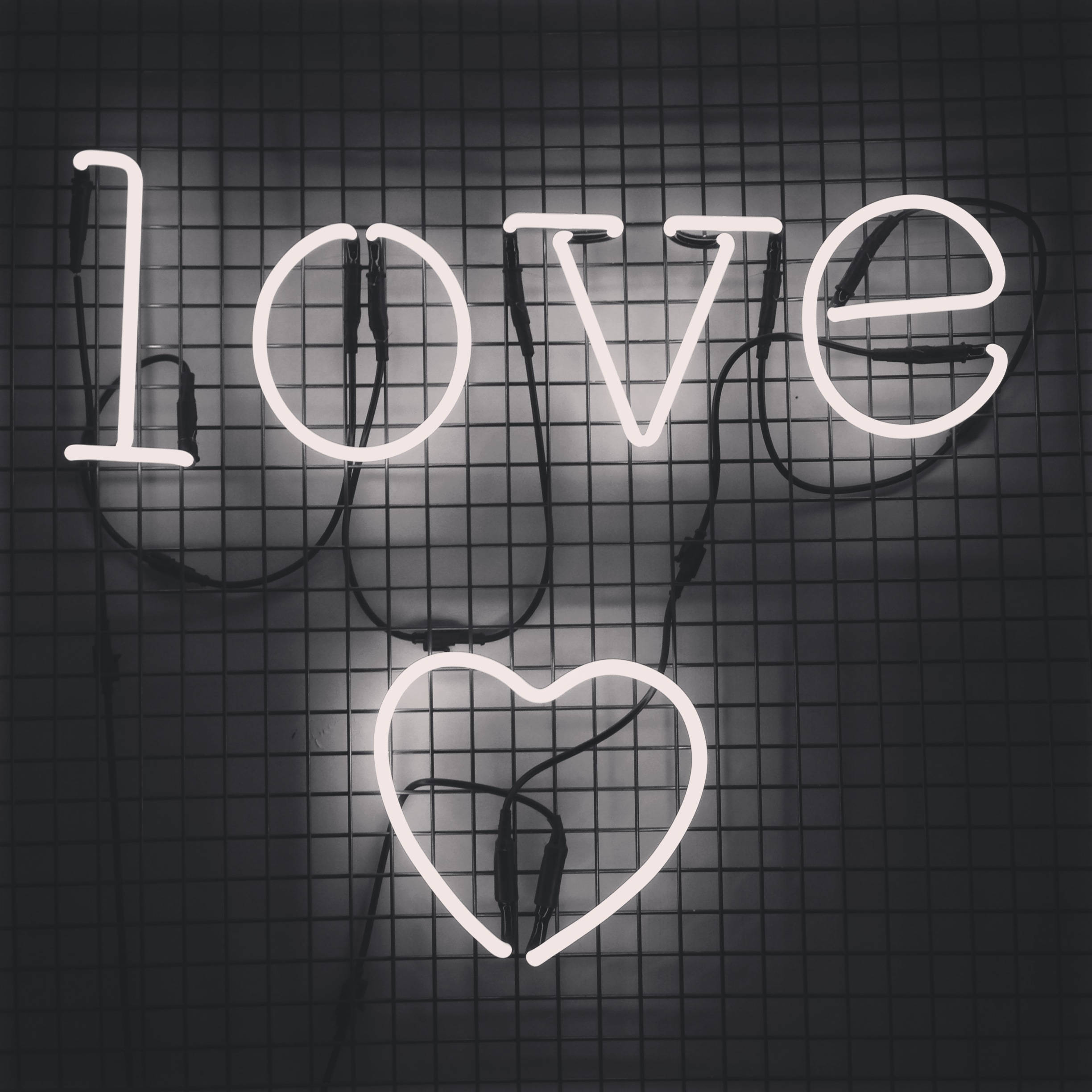 愛心 桌布 壁紙 — 一個發光的白色霓虹燈牌，拼出 'love'，下方有一個心形，安裝在深色格柵牆上。