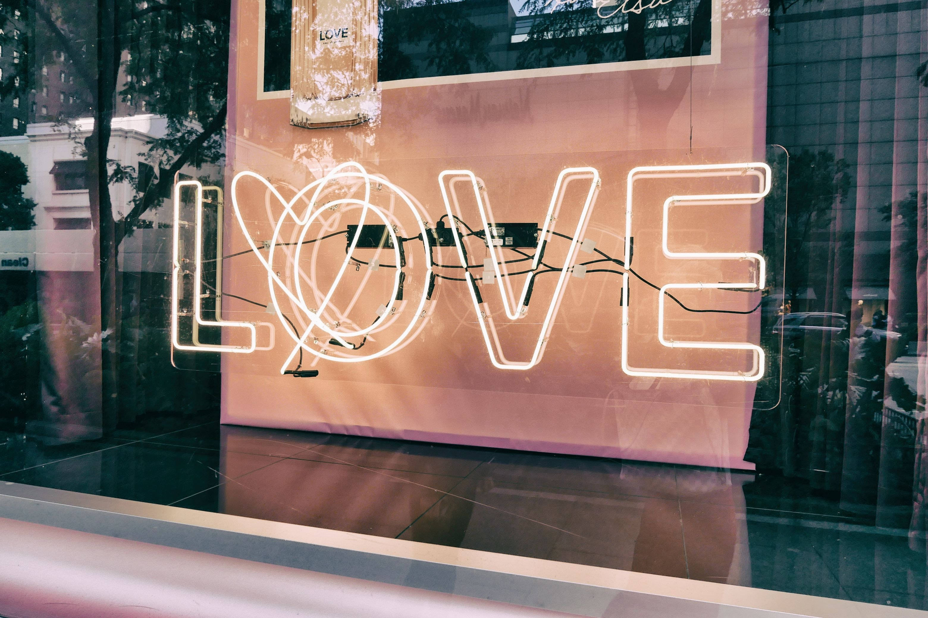 neon sign 桌布 壁紙 — 一個發光的白色霓虹燈牌，拼出LOVE，並以心形取代字母O，倒映在玻璃櫥窗上。
