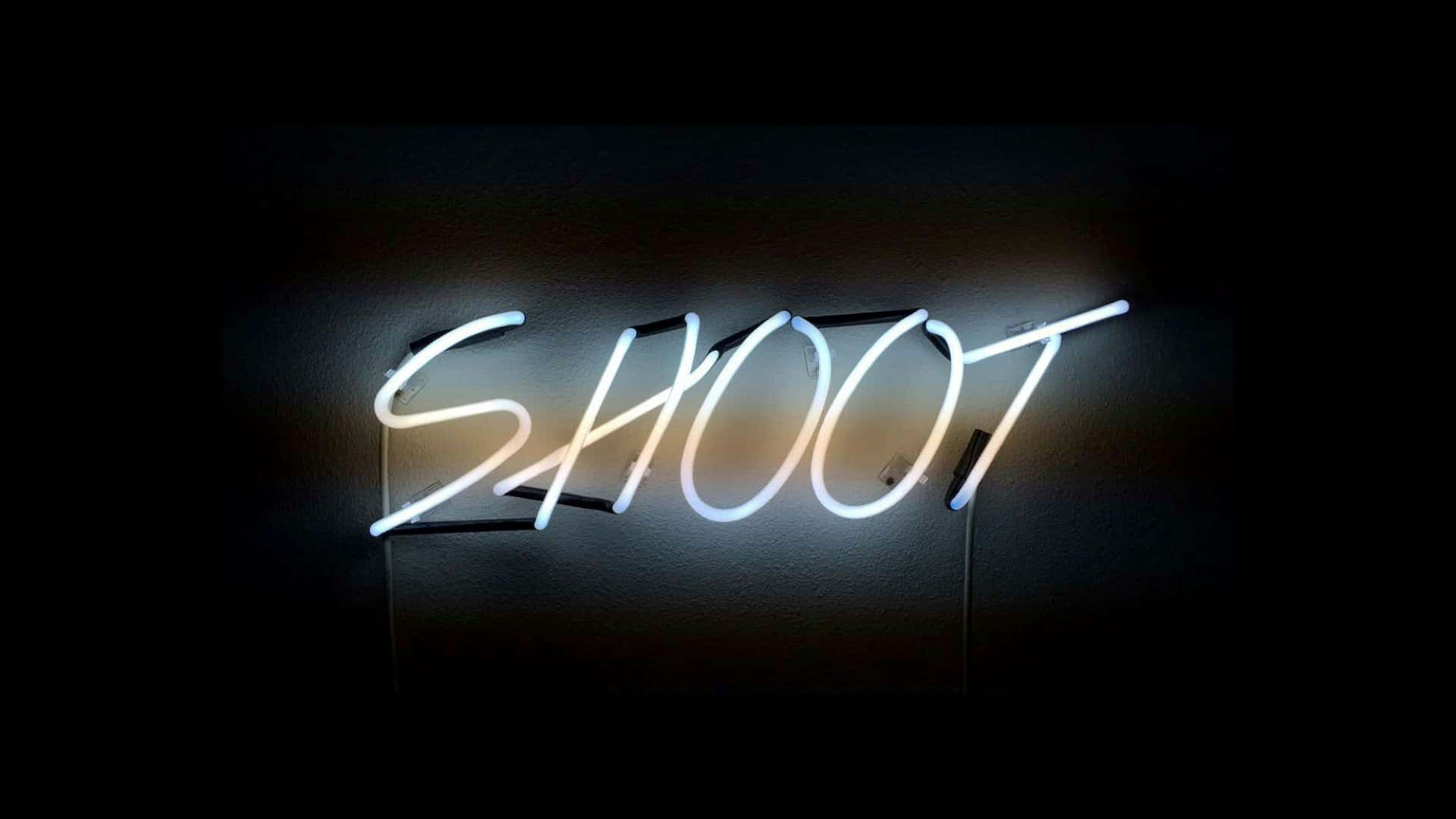 美學 桌布 壁紙 — 一個發光的白色霓虹燈牌，拼寫出 SHOOT，在昏暗的空間中將柔和的光線投射在深色牆壁上。