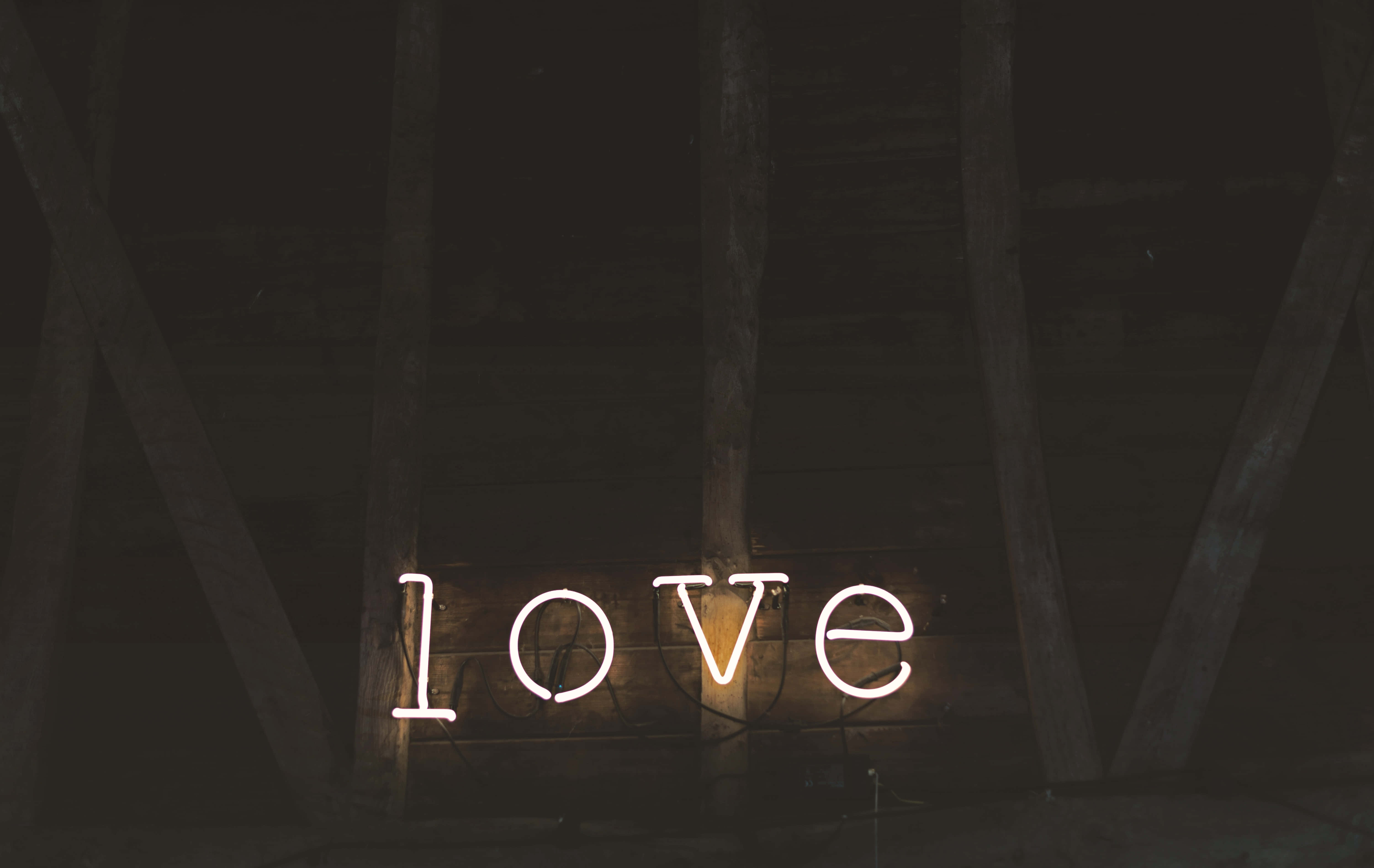 Dark Love 桌布 壁紙 — 一個發光的白色霓虹燈牌，拼寫著 love，掛在昏暗閣樓的深色木樑上。