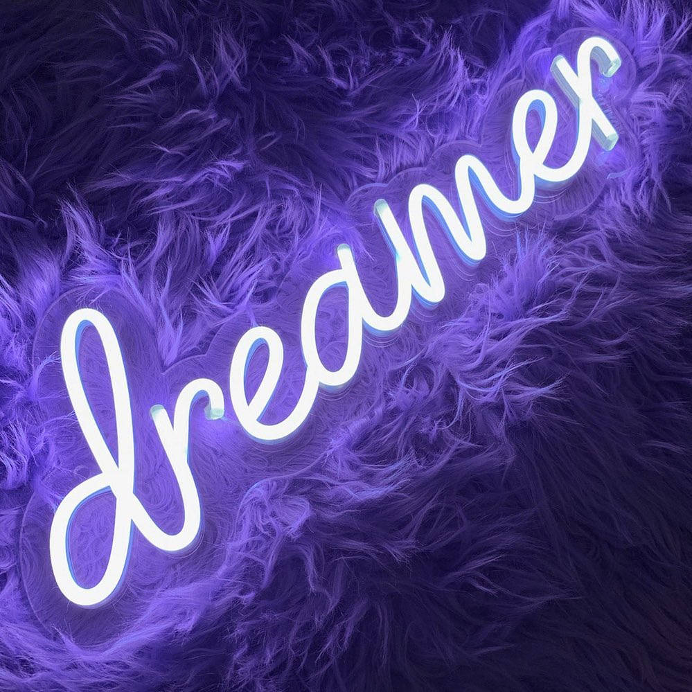 Light 桌布 壁紙 — 一個發光的白色霓虹燈牌，拼寫著 dreamer，放在柔軟的紫色毛絨表面上。