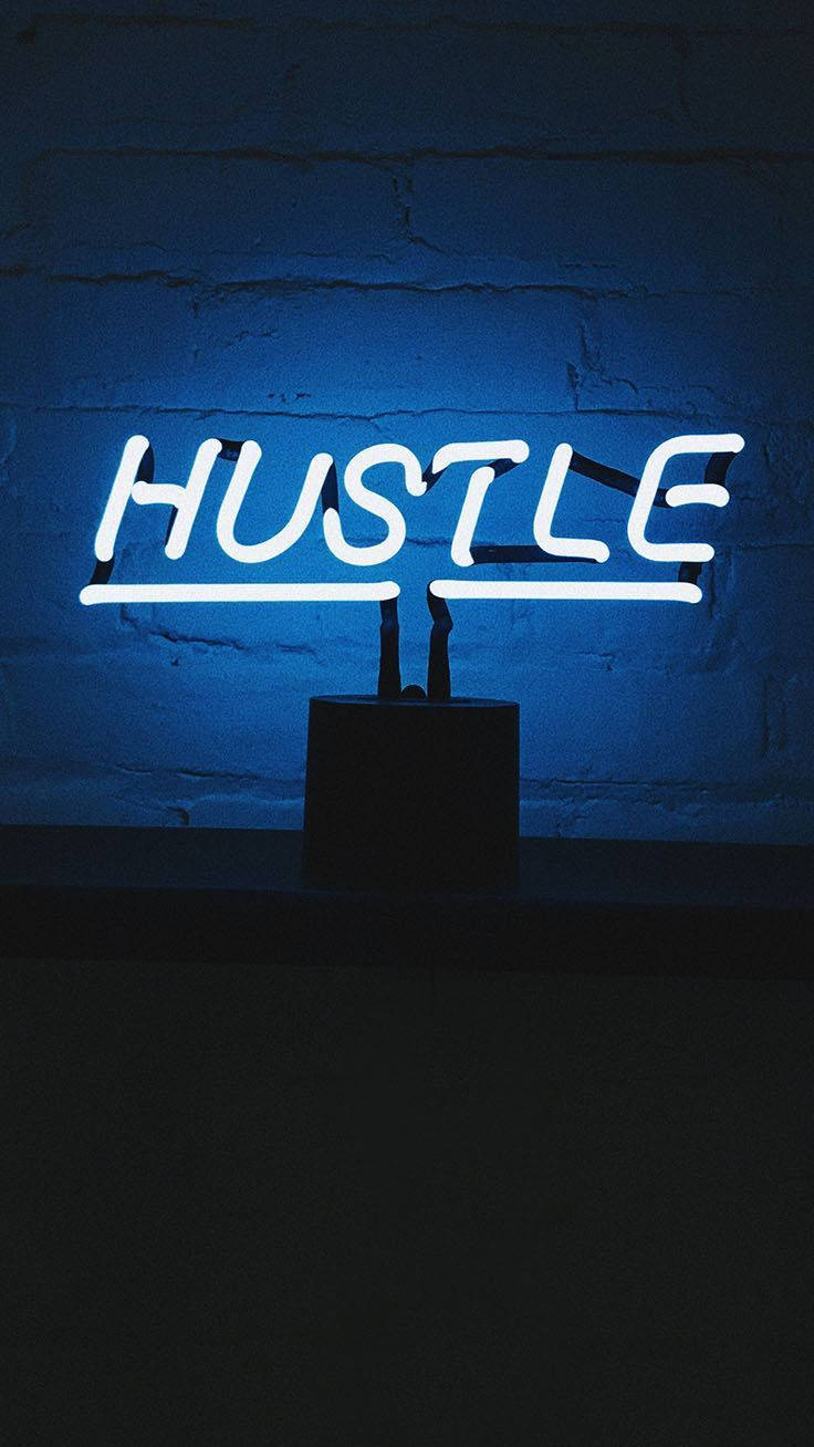 霓虹美學 桌布 壁紙 — 一個發光的白色霓虹燈牌，拼寫著 HUSTLE，在昏暗的空間中對著紋理磚牆投射出冷藍色的光芒。