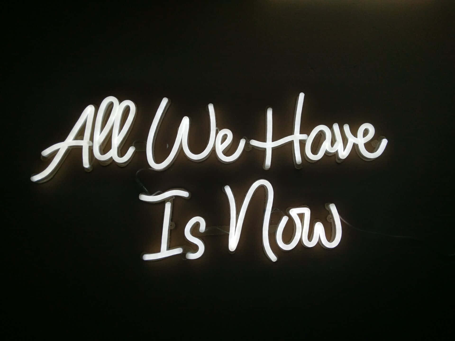 neon sign 桌布 壁紙 — 一個發光的白色霓虹燈牌在深色牆上顯示「All We Have Is Now」。