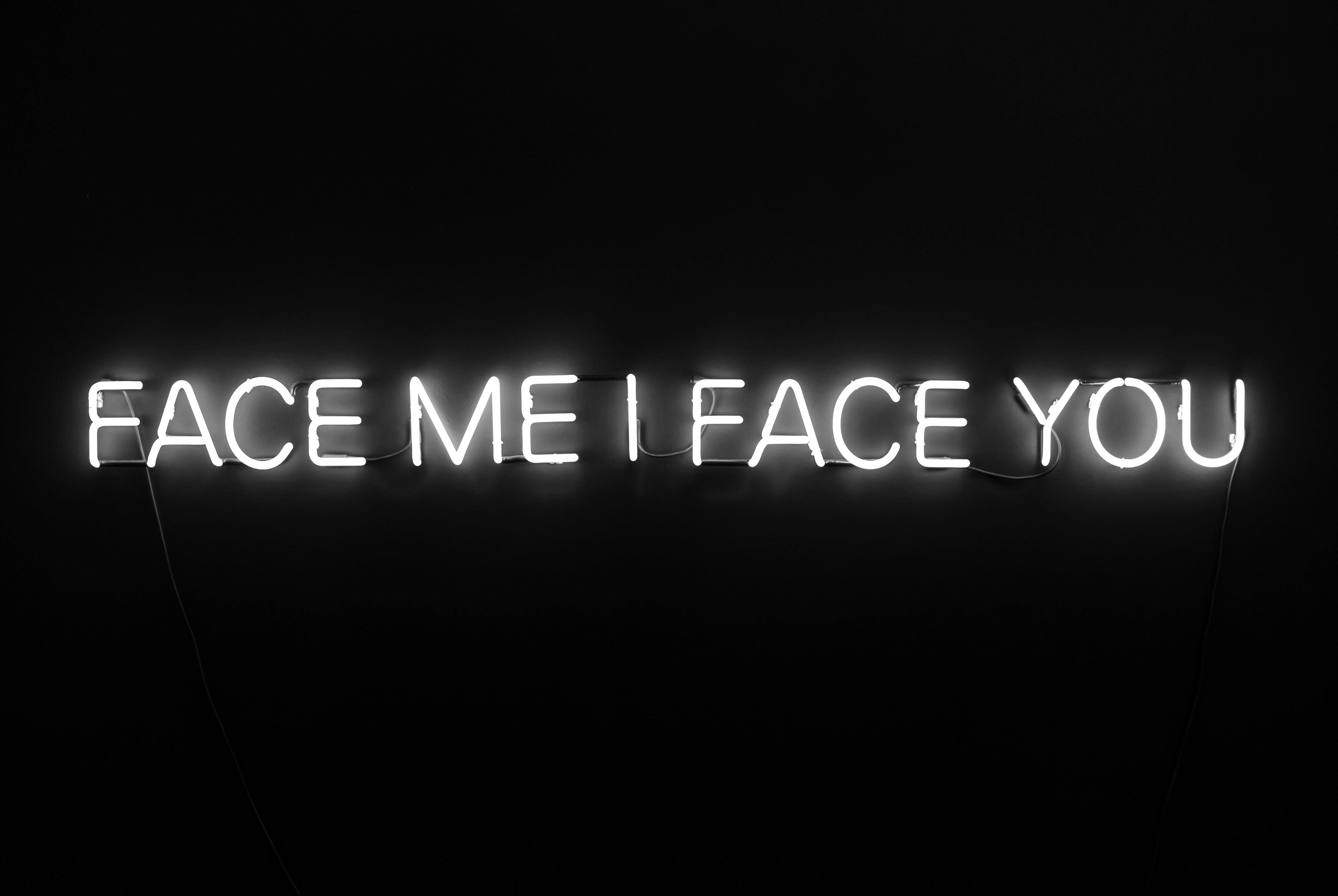 黑色 桌布 壁紙 — 一個發光的白色霓虹燈牌寫著 face me i face you，背景是漆黑的牆壁。