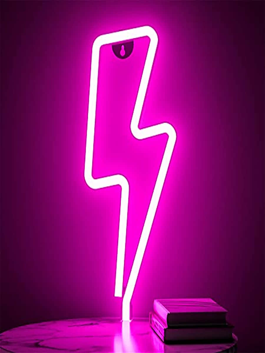 Neon Lightning 桌布 壁紙 — 一個發光的白色霓虹閃電標誌在大理石桌子上堆疊的書本旁邊的深色牆壁上投射出鮮豔的粉紅色光芒。