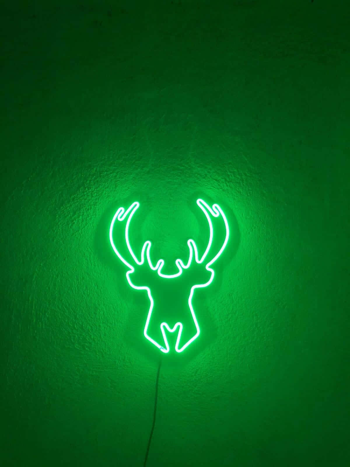 Milwaukee Bucks Logo 桌布 壁紙 — 一個發光的白色霓虹鹿頭剪影，在紋理深邃的綠色牆壁上投射出柔和的光芒。