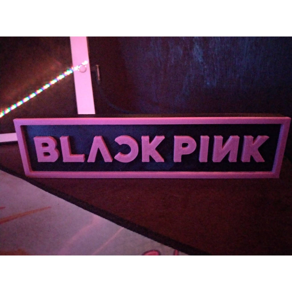 BLACKPINK 標誌 桌布 壁紙 — 一個發光的粉紅色3D標誌，上面寫著BLACK PINK，由彩色LED燈照亮，背景是深色木材。