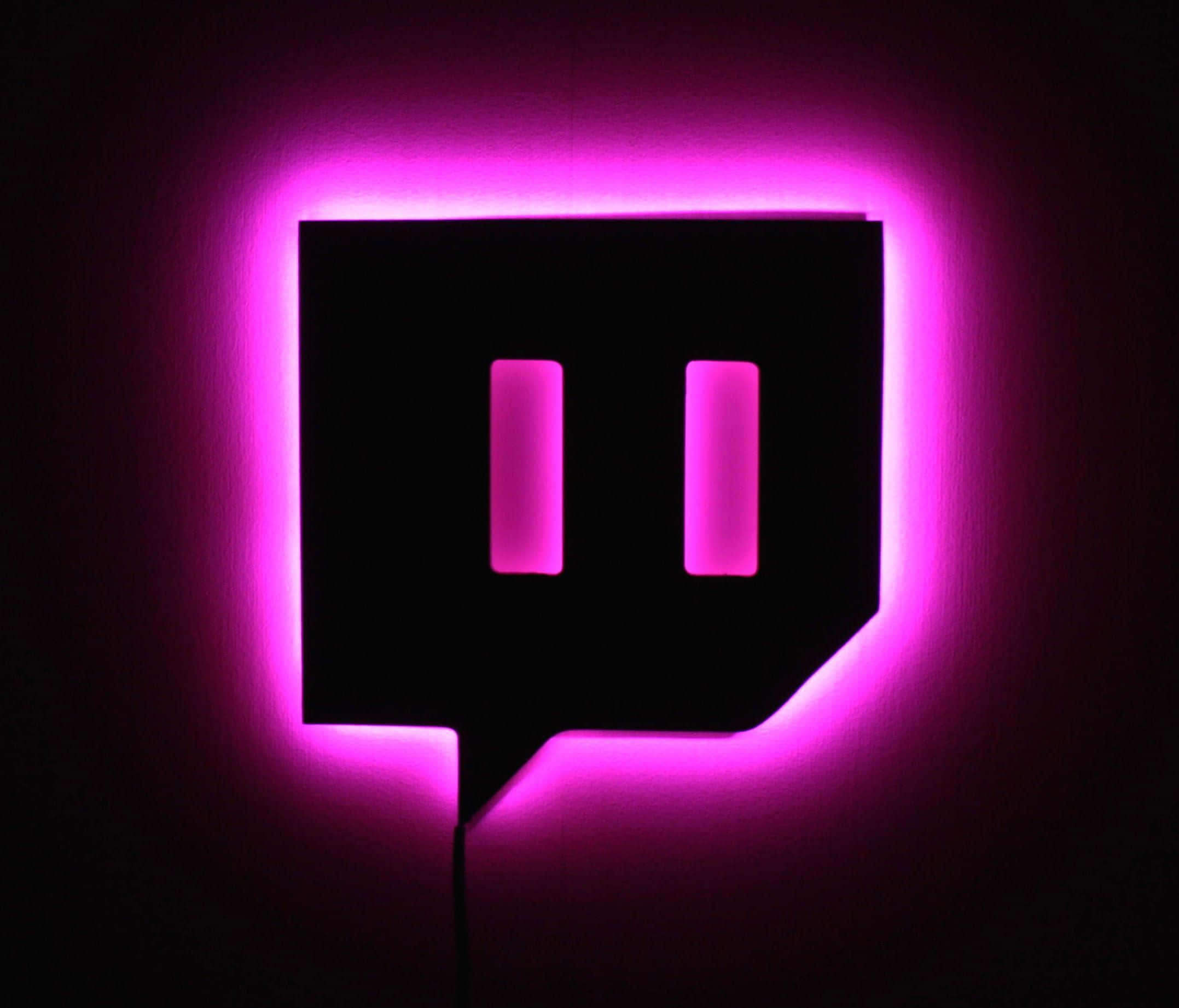 桌布 壁紙 — 一個發光的粉紅色Twitch標誌招牌在昏暗的房間中，在黑暗的牆壁上投射出充滿活力的霓虹光暈。