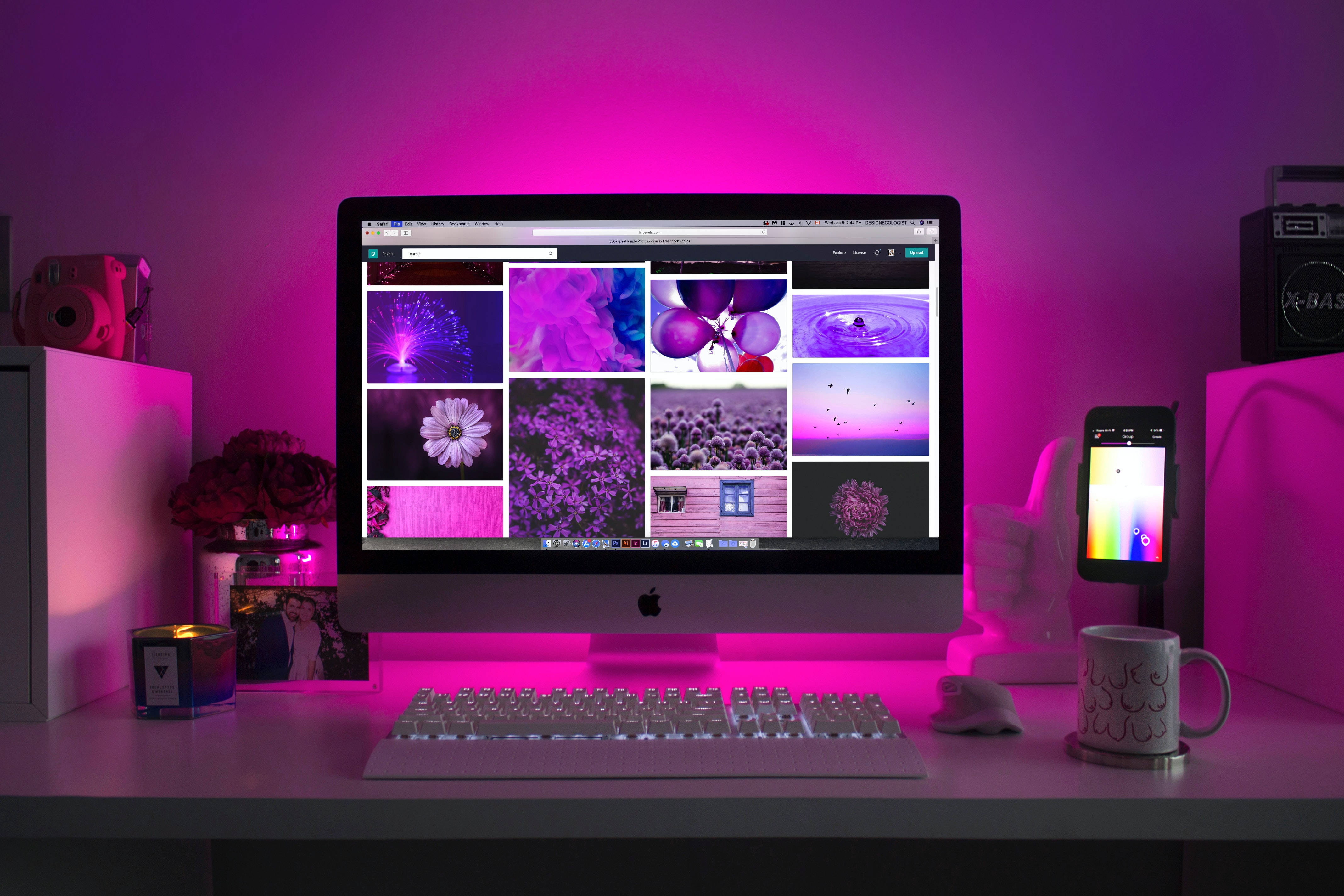 Computer Screen 桌布 壁紙 — 一個發光的粉紅色書桌設置，配備 iMac 顯示充滿活力的紫色壁紙畫廊，周圍環繞著科技小工具和裝飾。