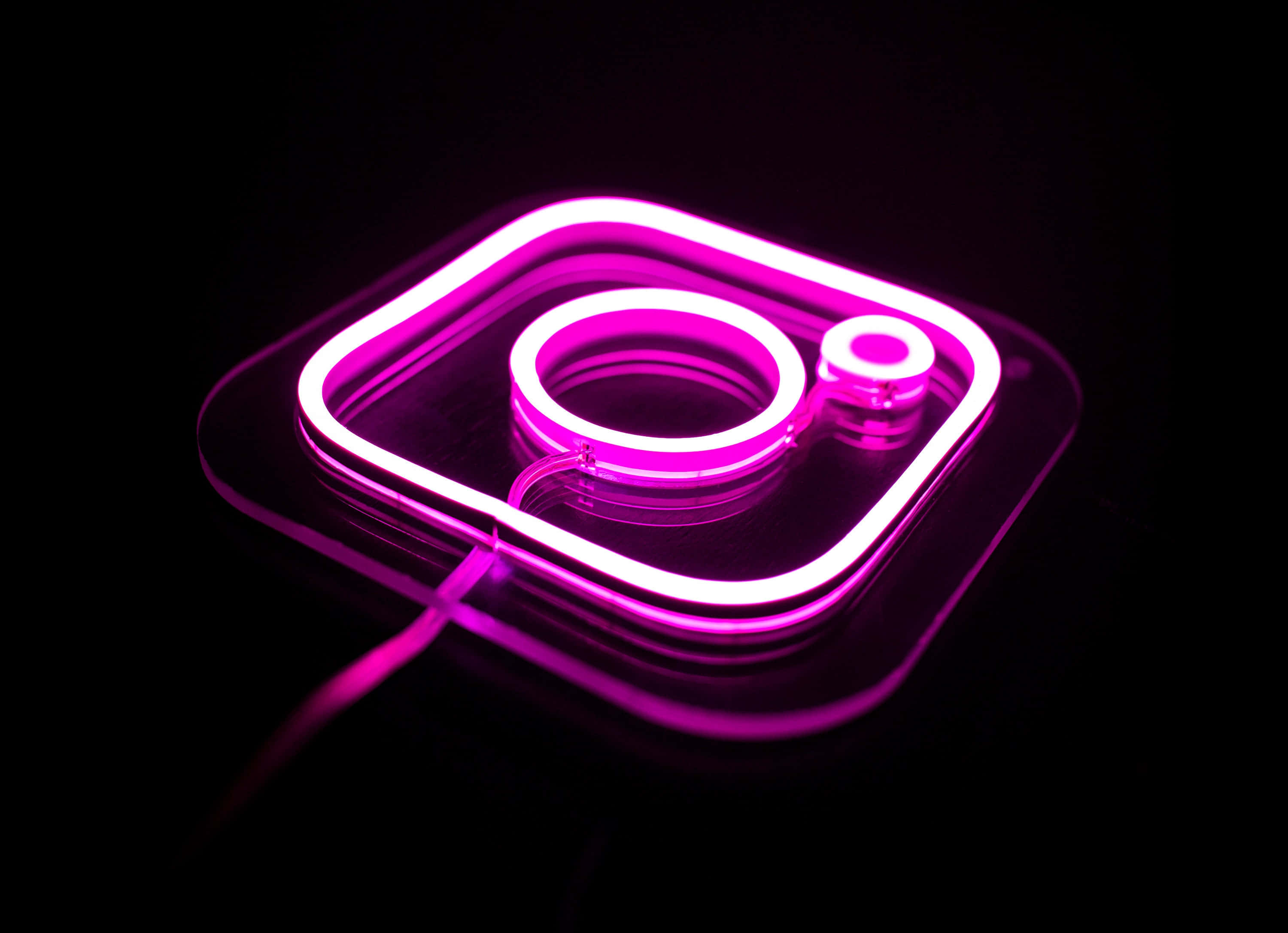 Instagram 桌布 壁紙 — 一個發光的粉紅色霓虹燈Instagram標誌招牌在深色光澤表面上投射出鮮豔的倒影。