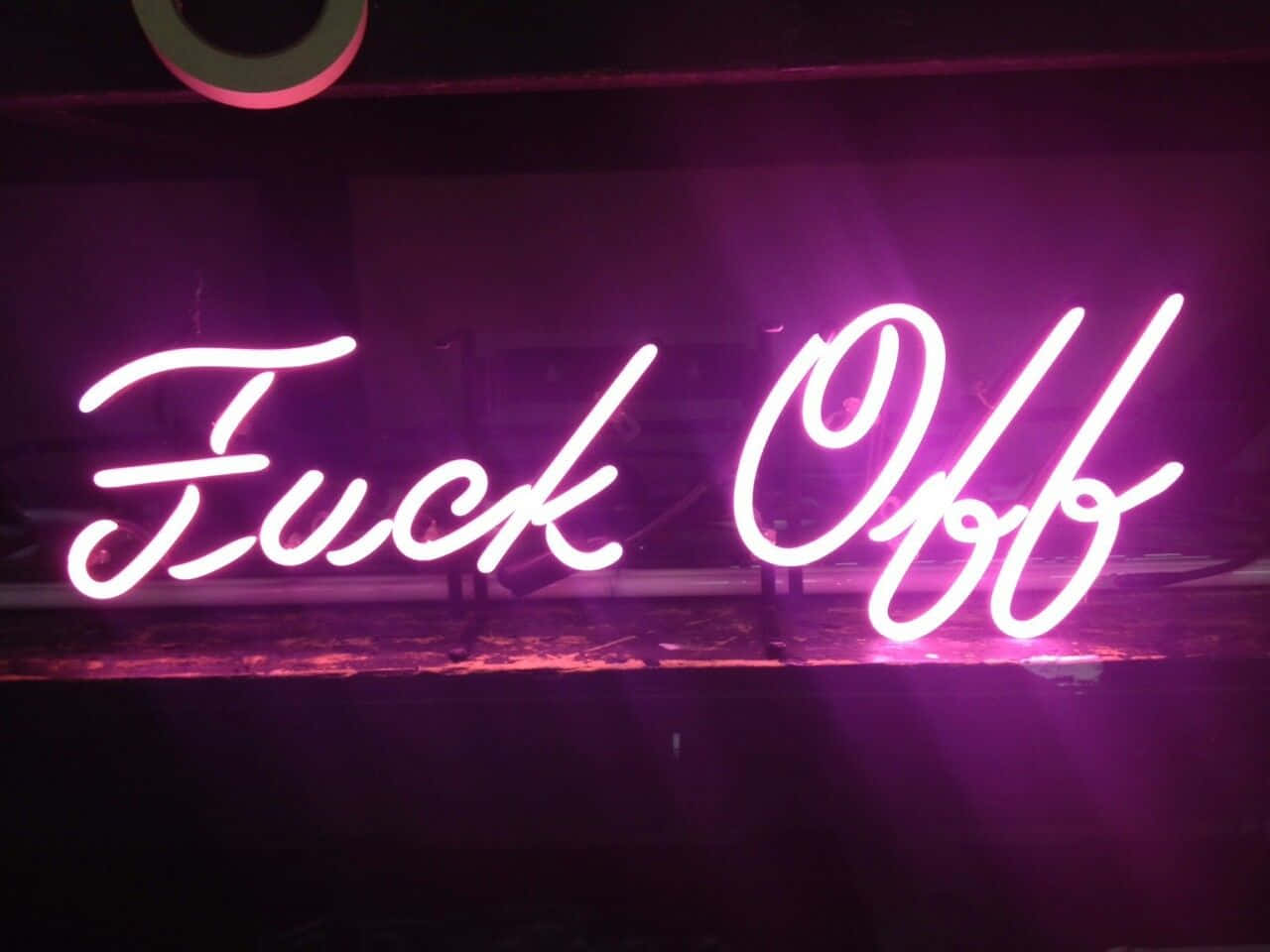 美學 桌布 壁紙 — 一個發光的粉紅色霓虹燈牌，上面以草書寫著 'Fuck Off'，照亮了黑暗、骯髒的城市室內。
