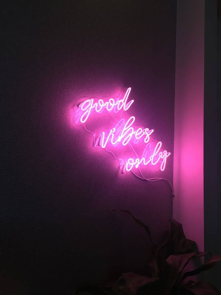 lights 桌布 壁紙 — 一個發光的粉紅色霓虹燈牌，上面寫著 good vibes only，在植物旁邊的暗牆上投射出柔和的光線。