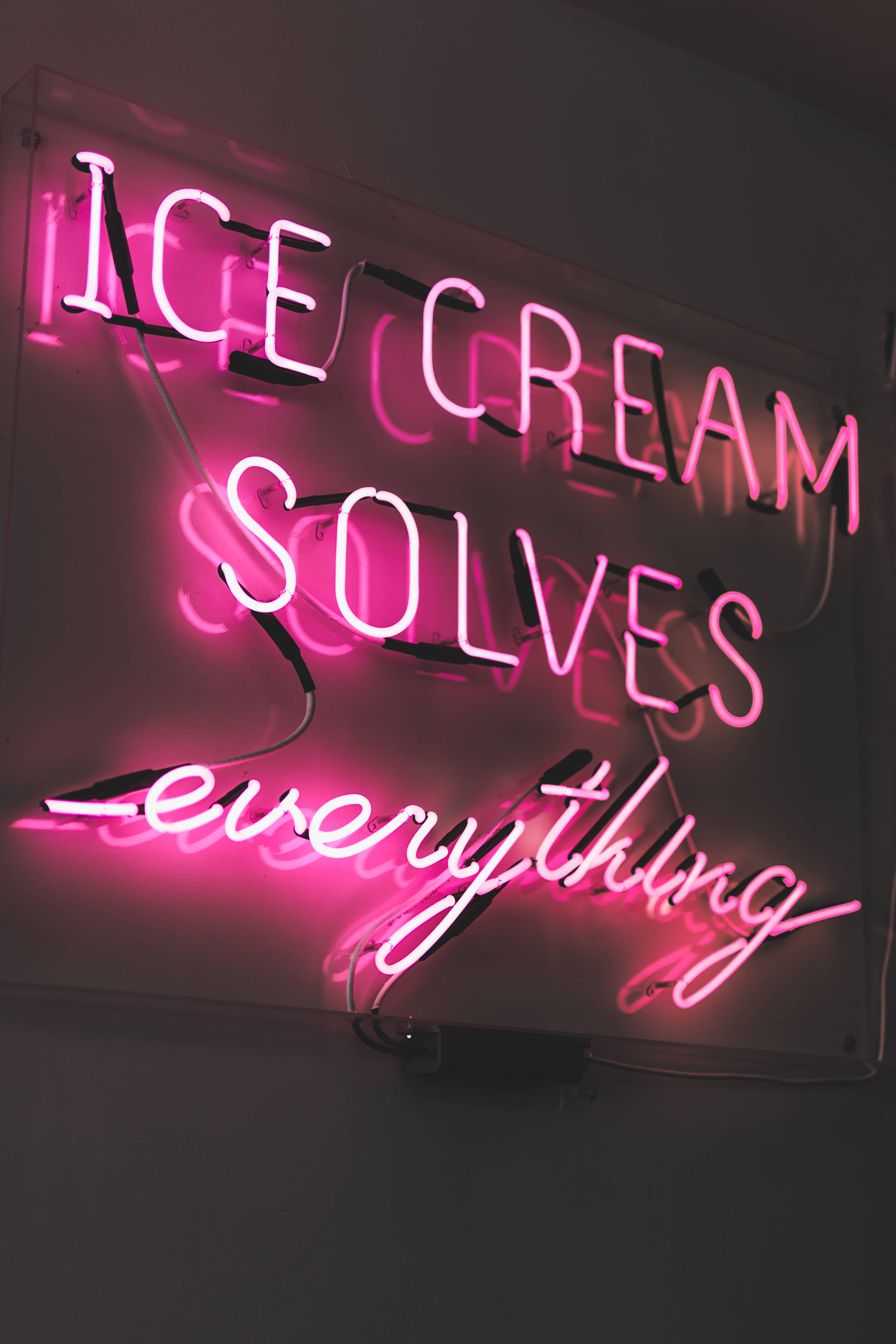 語錄 桌布 壁紙 — 一個發光的粉紅色霓虹燈牌，上面寫著 ice cream solves everything，背景是深色牆壁。