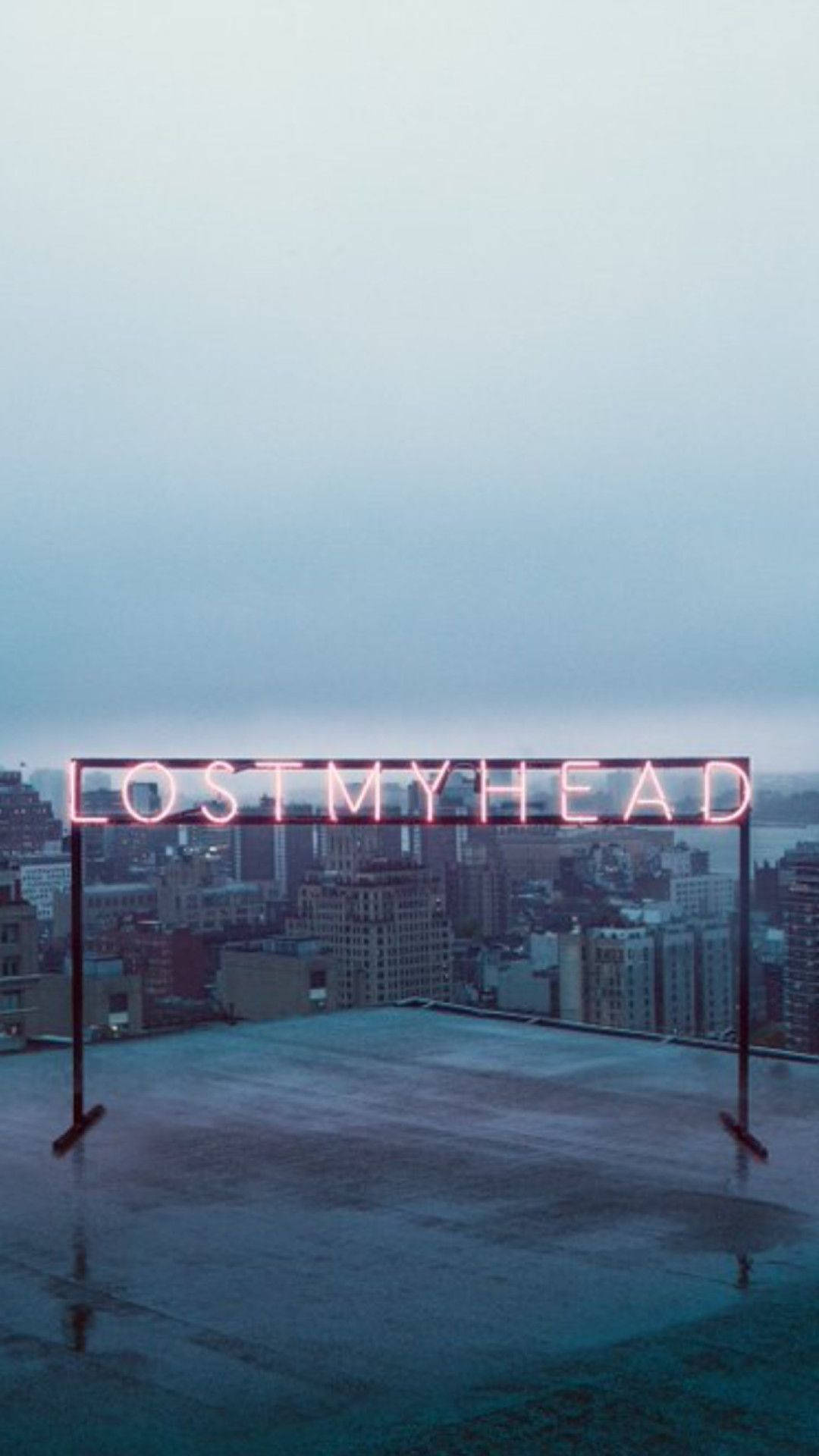 Lo Fi iPhone 桌布 壁紙 — 一個發光的粉紅色霓虹燈牌，上面寫著 lostmyhead，矗立在一個濕漉漉的屋頂上，俯瞰著黃昏時分朦朧的城市天際線。