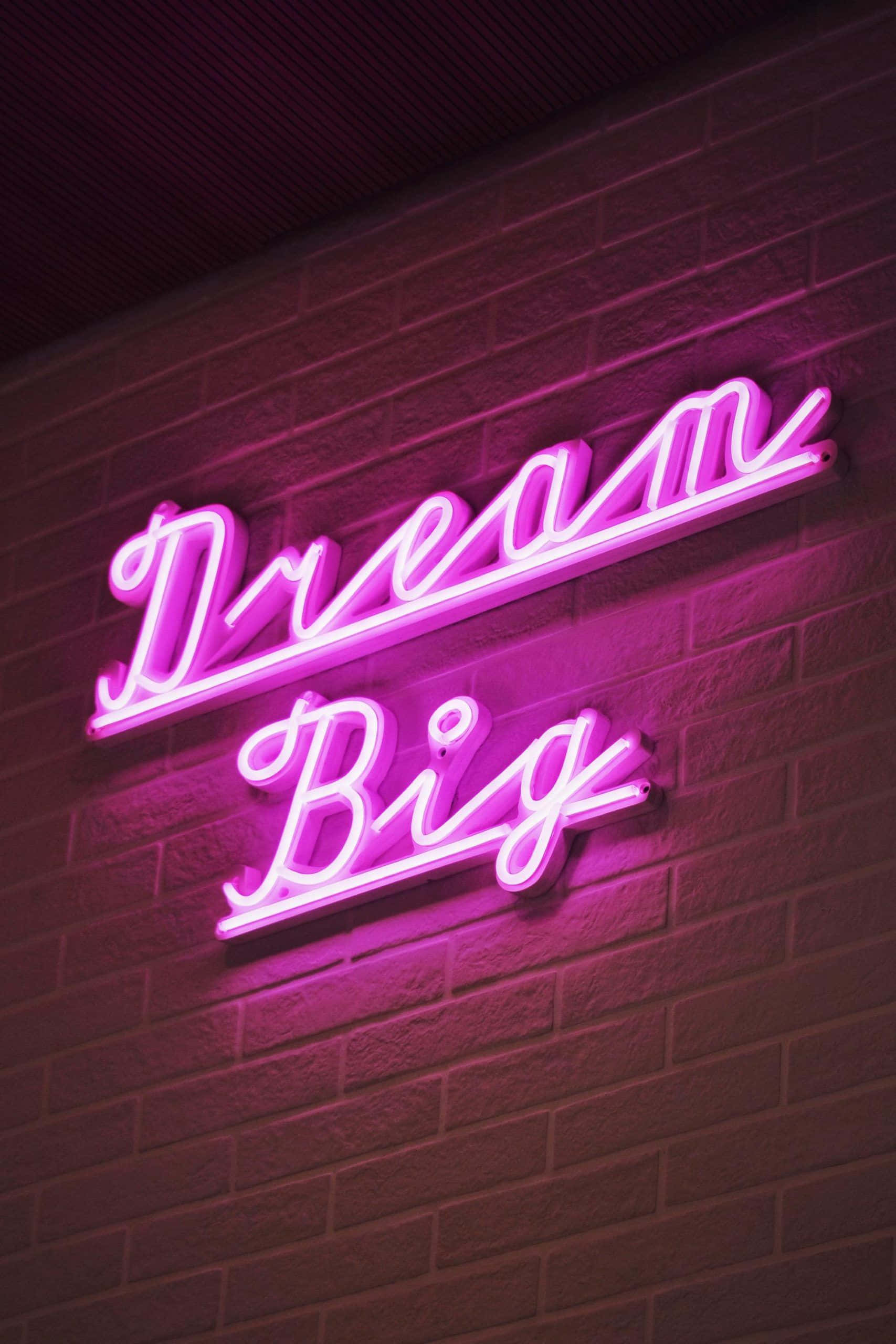 霓虹美學 桌布 壁紙 — 一個發光的粉紅色霓虹燈牌，上面寫著「Dream Big」，在昏暗的空間中將鮮豔的色彩投射在紋理磚牆上。