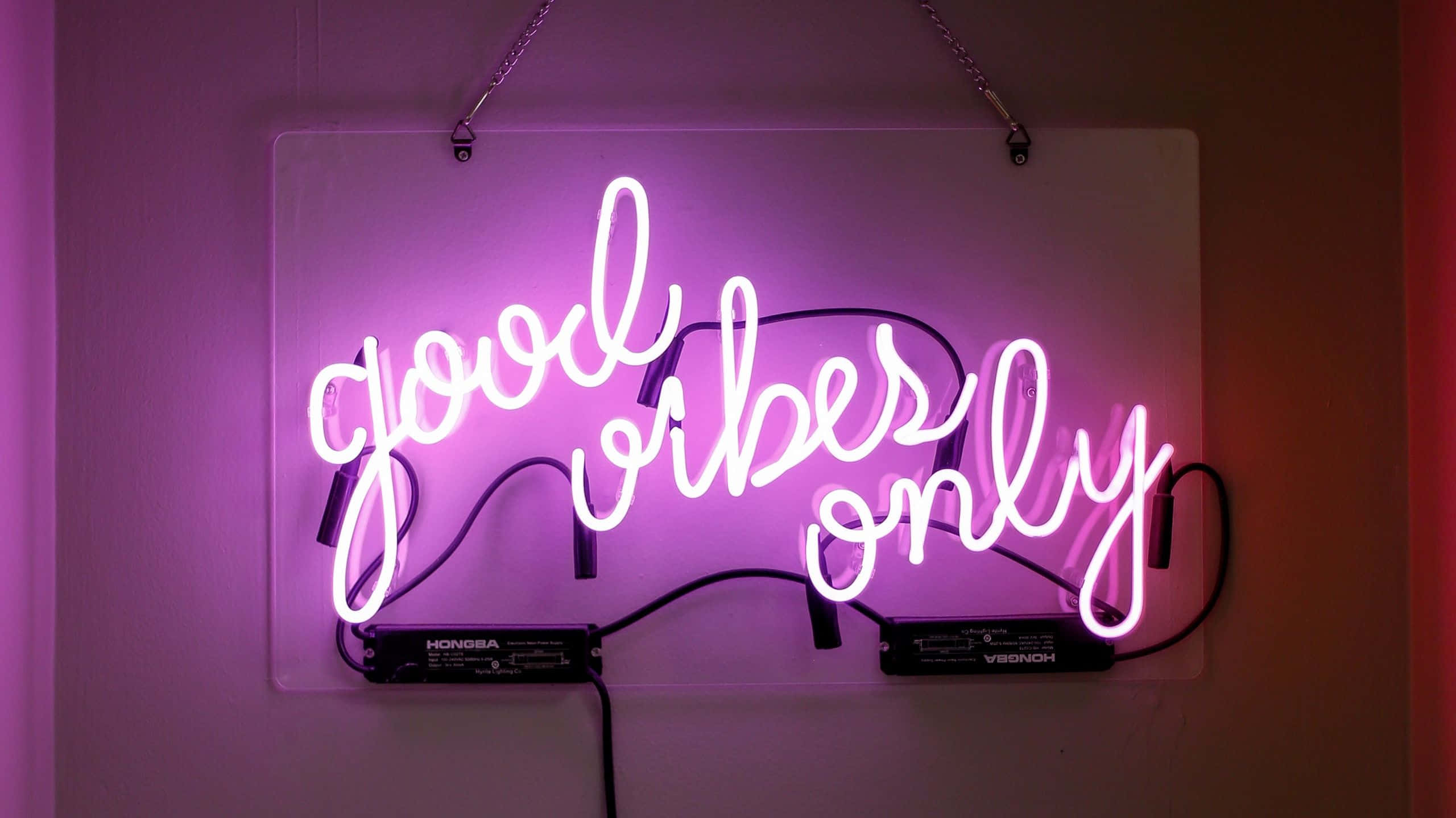 粉紅色系 桌布 壁紙 — 一個發光的粉紅色霓虹燈牌，上面寫著「good vibes only」，掛在牆上，投射出柔和的紫色光。