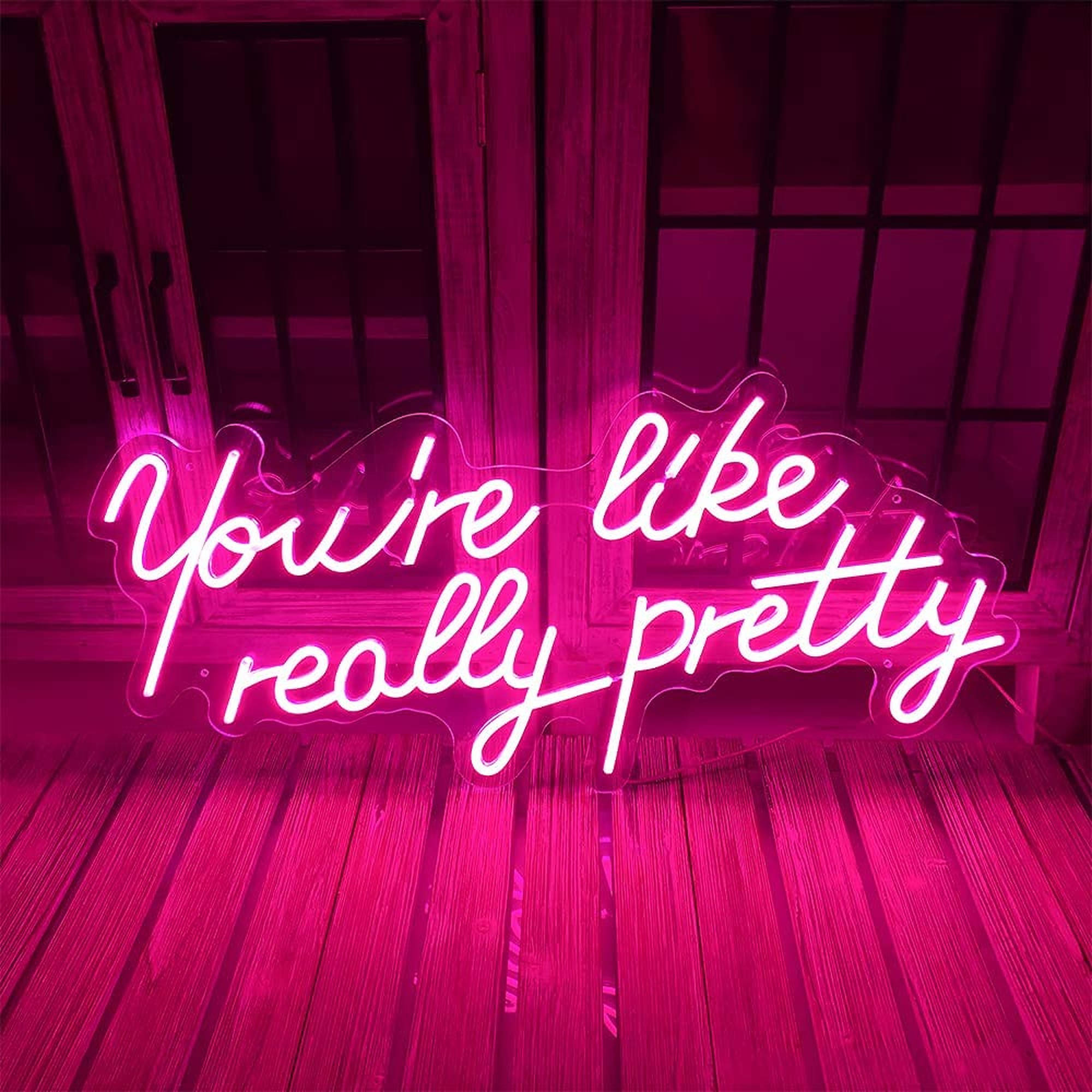 LED 桌布 壁紙 — 一個發光的粉紅色霓虹燈牌，上面寫著「You're like really pretty」，在昏暗的房間中將鮮豔的色彩投射在木地板和玻璃門上。