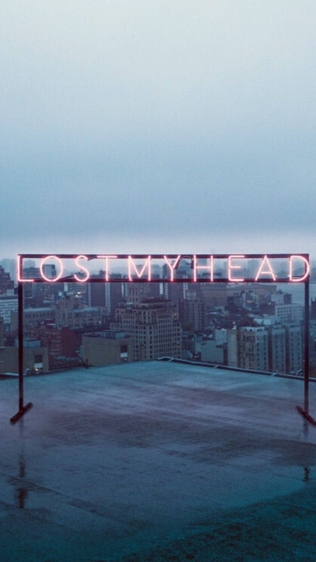 美學平板 桌布 壁紙 — 一個發光的粉紅色霓虹燈牌，上面寫著 lost my head，矗立在一個濕漉漉的屋頂上，俯瞰著黃昏時分朦朧的城市景觀。