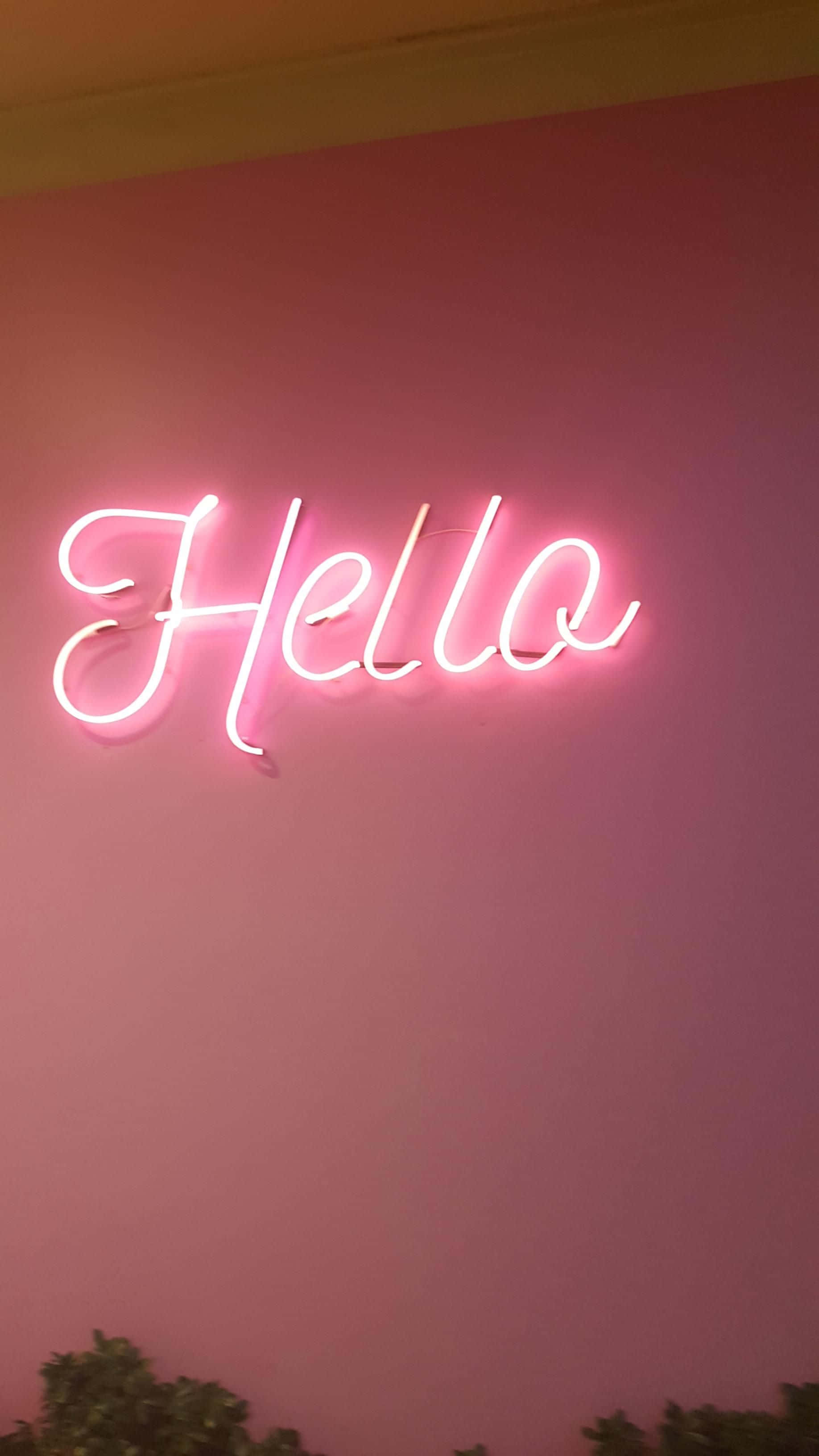 Cute Neon Pink 桌布 壁紙 — 一個發光的粉紅色霓虹燈牌，上面寫著「Hello」，在底部有綠色植物的粉紅色牆壁上投射出柔和的光線。