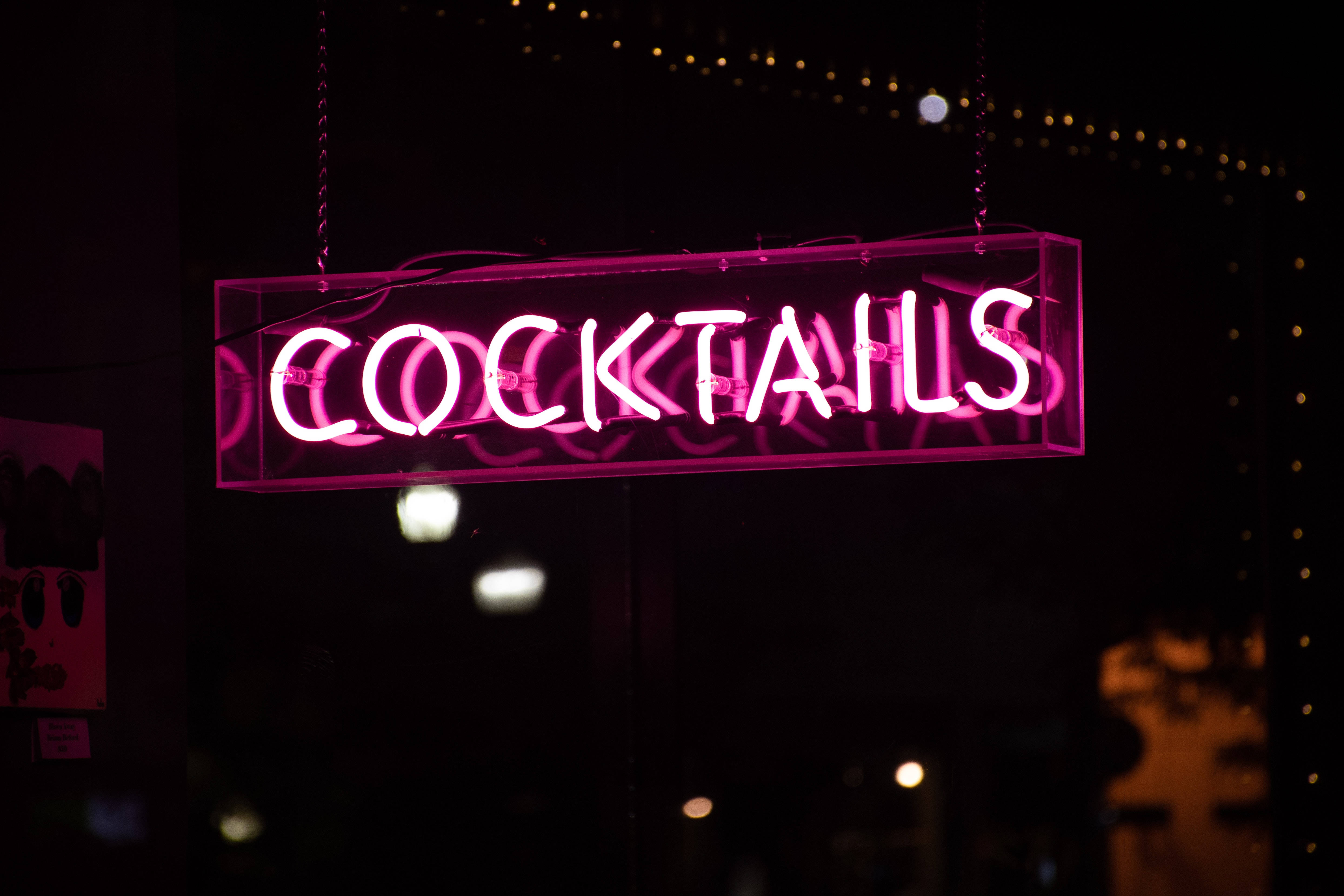 neon sign 桌布 壁紙 — 一個發光的粉紅色霓虹燈牌寫著 cocktails 懸掛在黑暗中，背景有散景燈光。