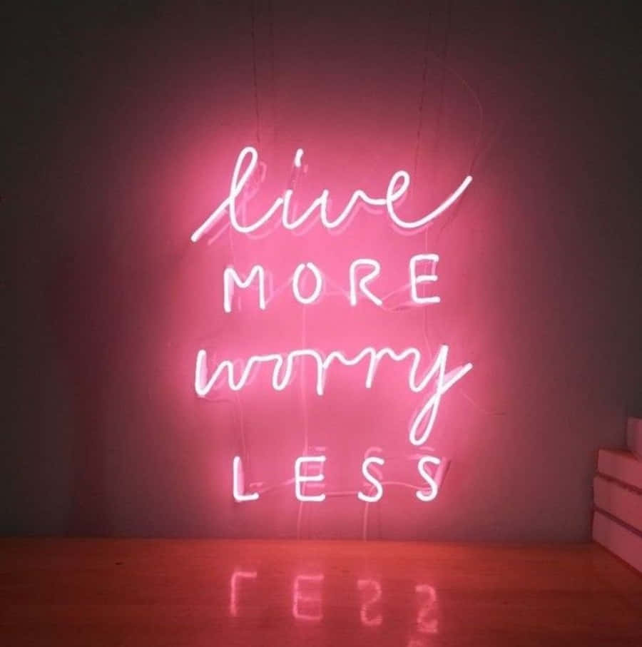 Quote 桌布 壁紙 — 一個發光的粉紅色霓虹燈牌寫著 live more worry less，在昏暗的房間中於木地板上投射出溫暖的倒影。