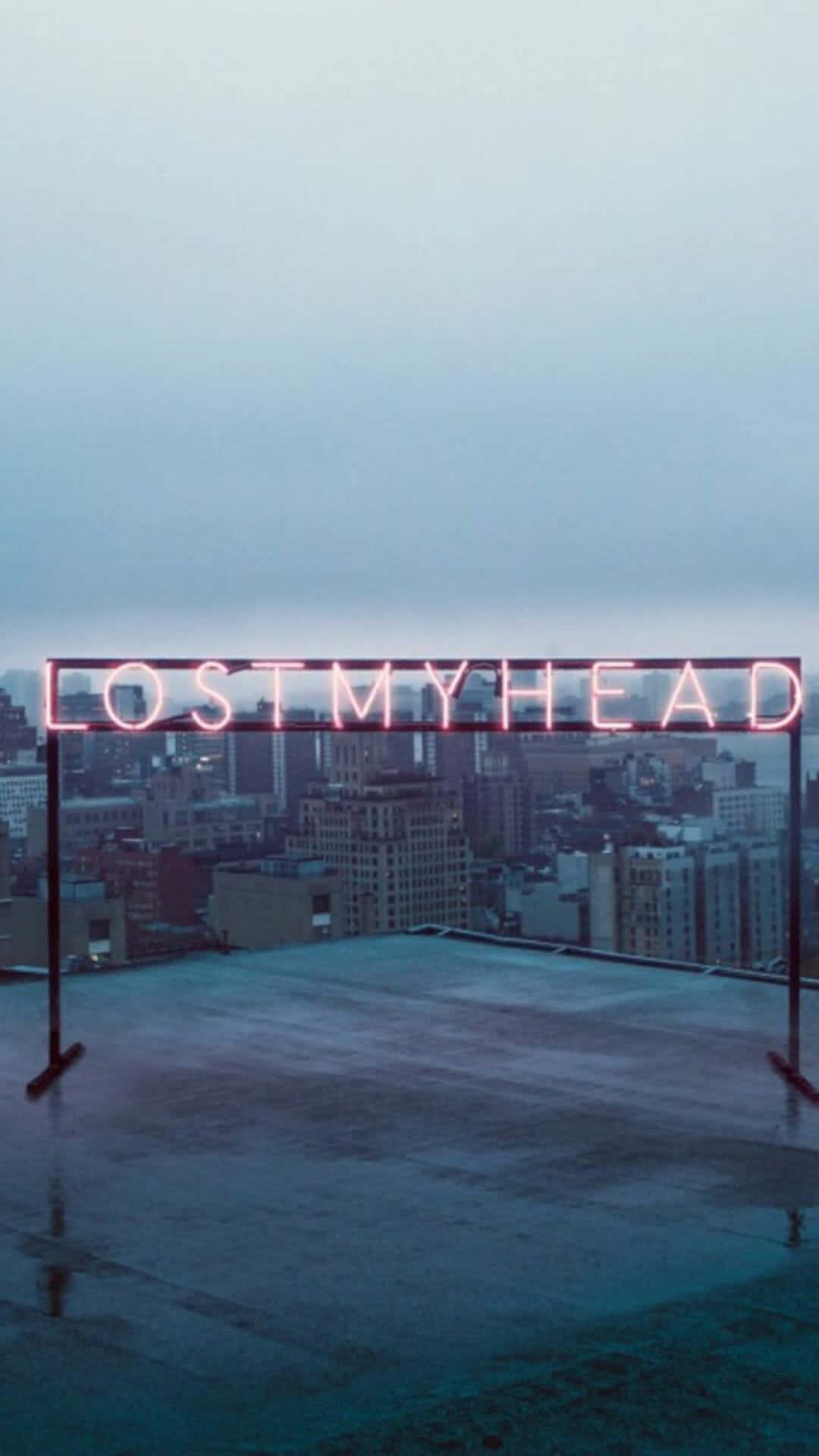 桌布 壁紙 — 一個發光的粉紅色霓虹燈牌寫著 lost my head，矗立在濕漉漉的屋頂上，俯瞰黃昏時分朦朧的城市天際線。