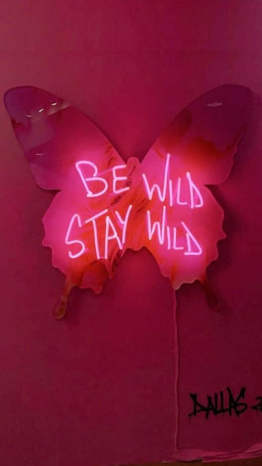 桌布 壁紙 — 一個發光的粉紅色霓虹燈蝴蝶標誌，上面寫著「BE WILD STAY WILD」，安裝在相配的粉紅色牆壁上。