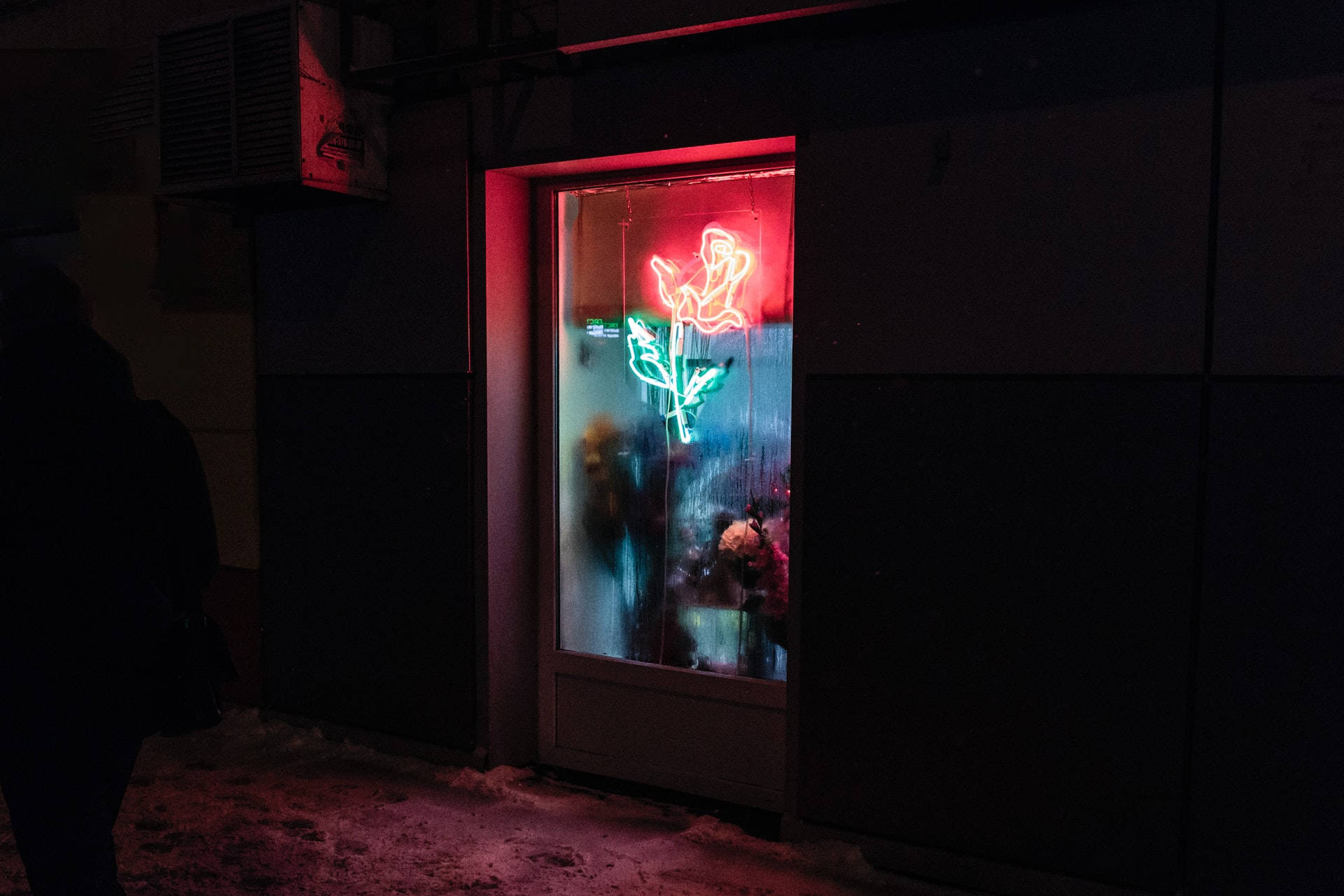 Night Aesthetic 桌布 壁紙 — 一個發光的紅綠霓虹玫瑰標誌照亮了雪夜中結霜的商店櫥窗。