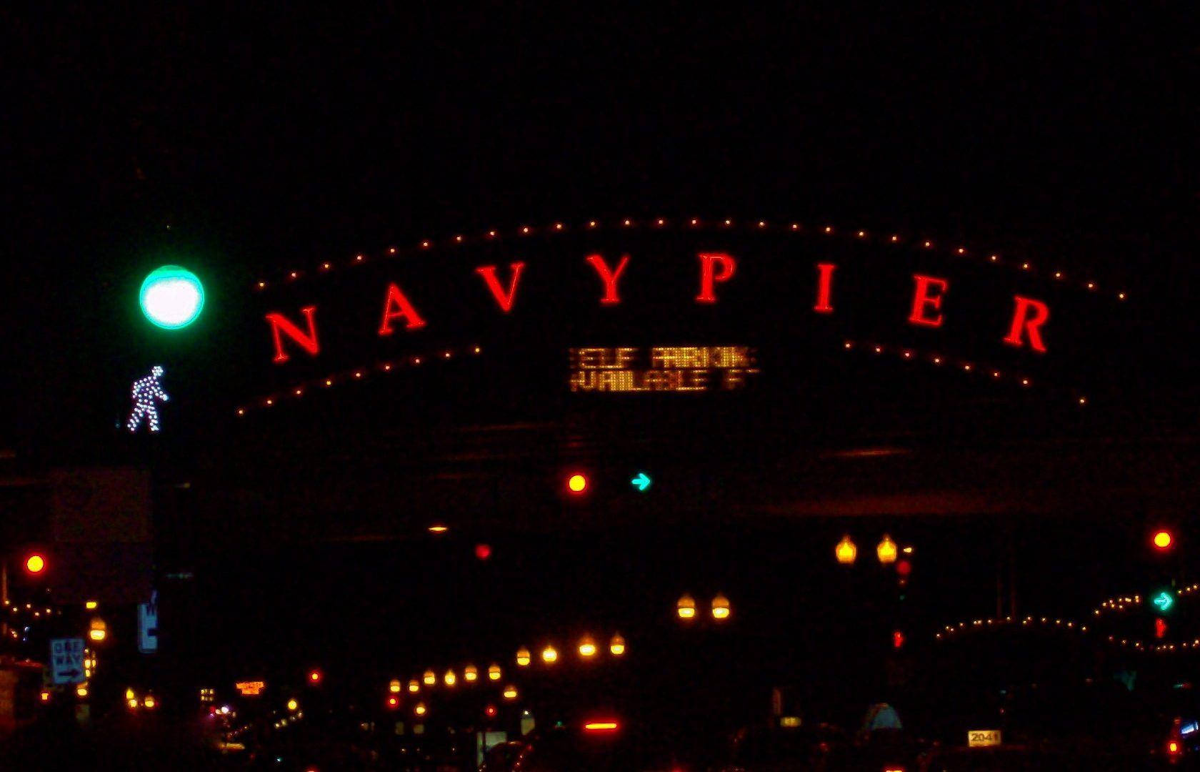 夜空 桌布 壁紙 — 一個發光的紅色「NAVY PIER」標誌拱形橫跨在黑暗的夜景上，散落著街燈和一個綠色行人信號燈。