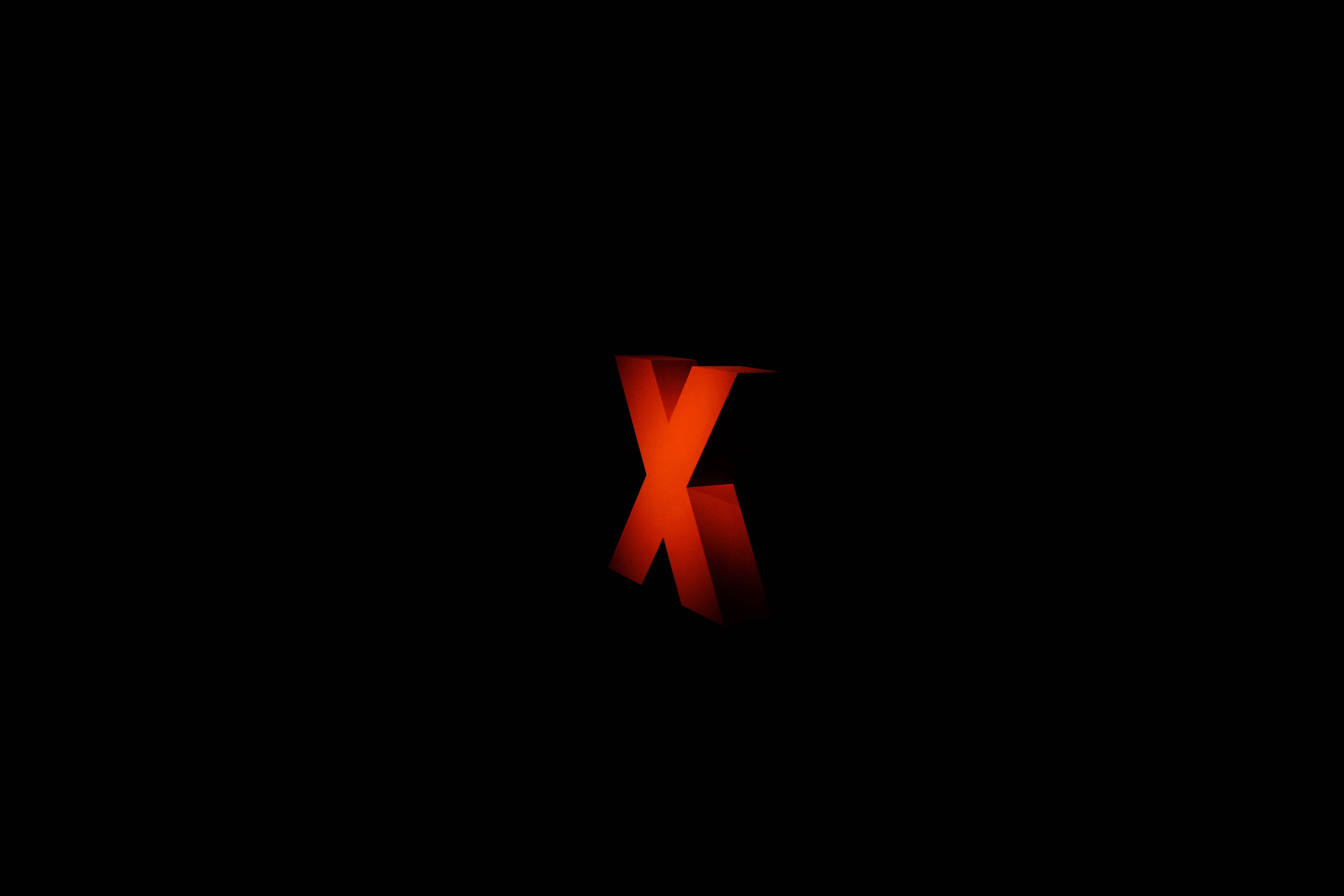 X 桌布 壁紙 — 一個發光的紅色3D字母X居中立在純黑色背景上，柔和的光線突出其邊緣。