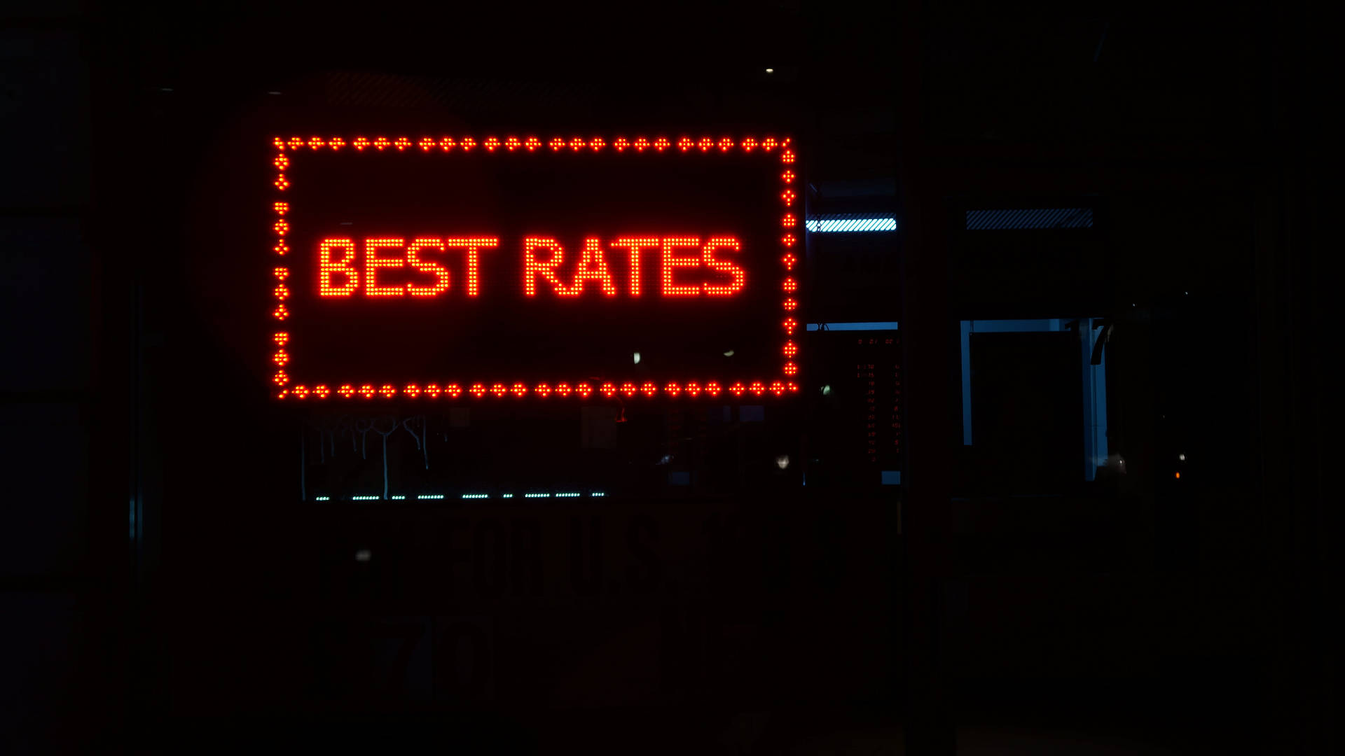 金錢 桌布 壁紙 — 一個發光的紅色LED招牌，上面寫著「BEST RATES」，照亮了黑暗的城市夜景，背景中有微弱的藍色燈光。