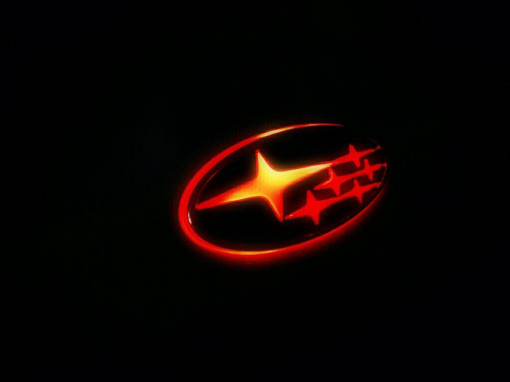 Subaru Logo 桌布 壁紙 — 一個發光的紅色Subaru標誌，橢圓形內有一顆明亮的星星和較小的星星，置於純黑色背景上。
