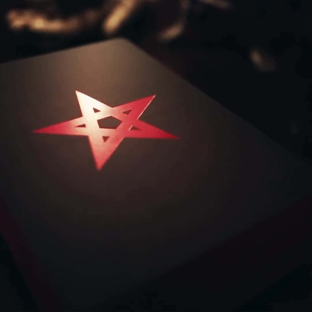 Thelema 桌布 壁紙 — 一個發光的紅色五角星符號放置在深色紋理表面上，處於戲劇性的低光照明下。