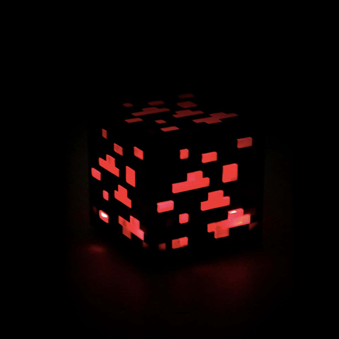 Minecraft Redstone 桌布 壁紙 — 一個發光的紅色像素立方體在漆黑背景上散發出溫暖的光芒，投射出柔和的陰影。