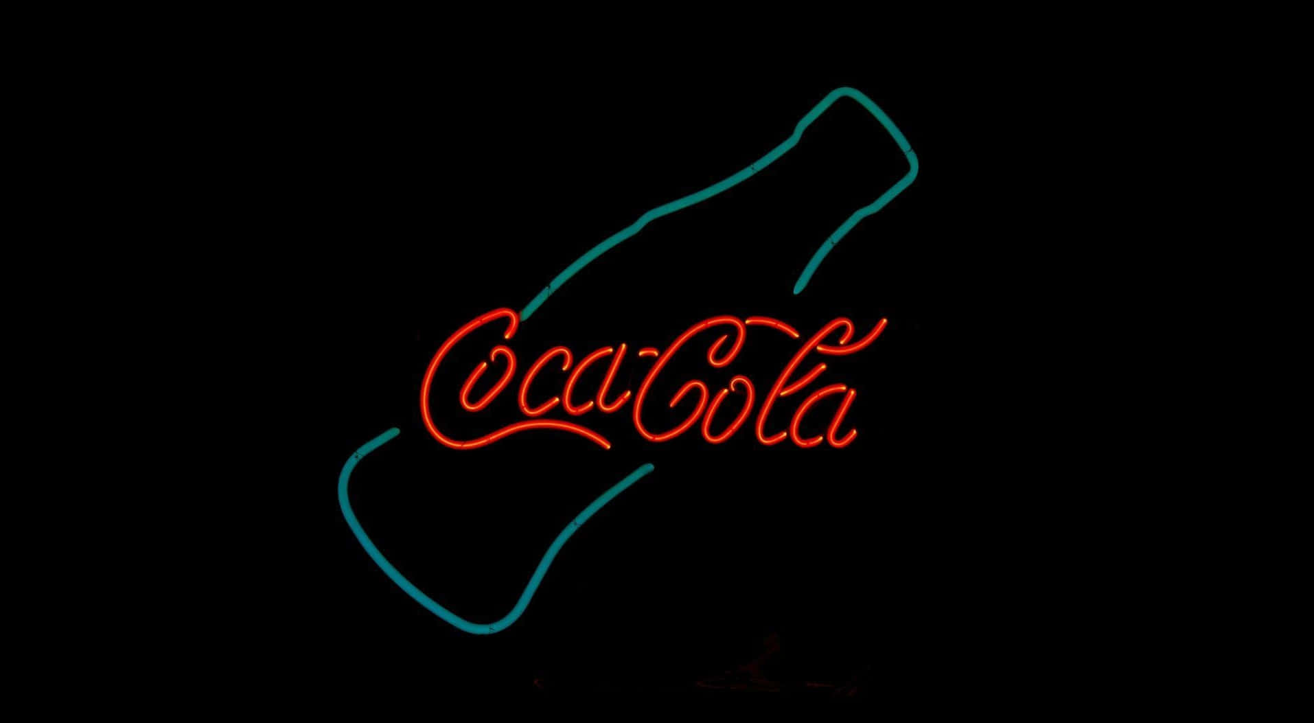 coca cola 桌布 壁紙 — 一個發光的紅色和藍綠色霓虹燈標誌，形狀像可口可樂瓶，背景為黑色。