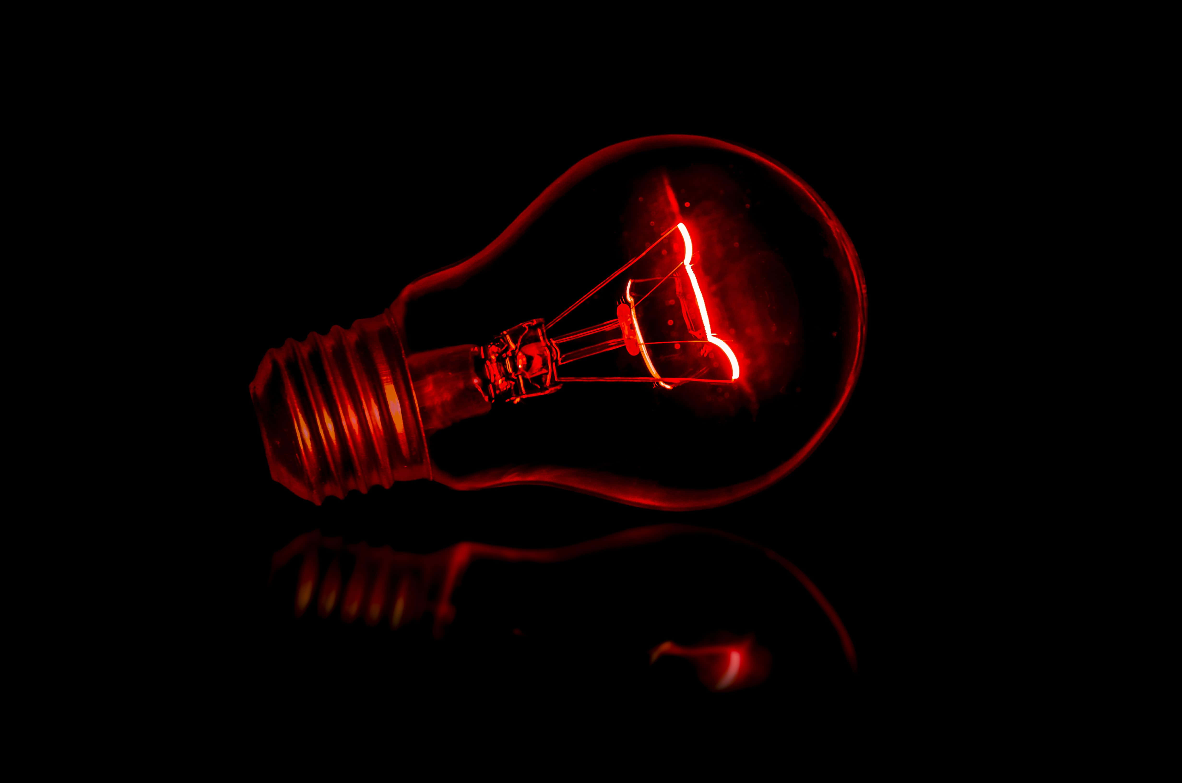 Bulb 桌布 壁紙 — 一個發光的紅色復古燈泡在黑色背景下的暗色表面上投射出溫暖的反射。