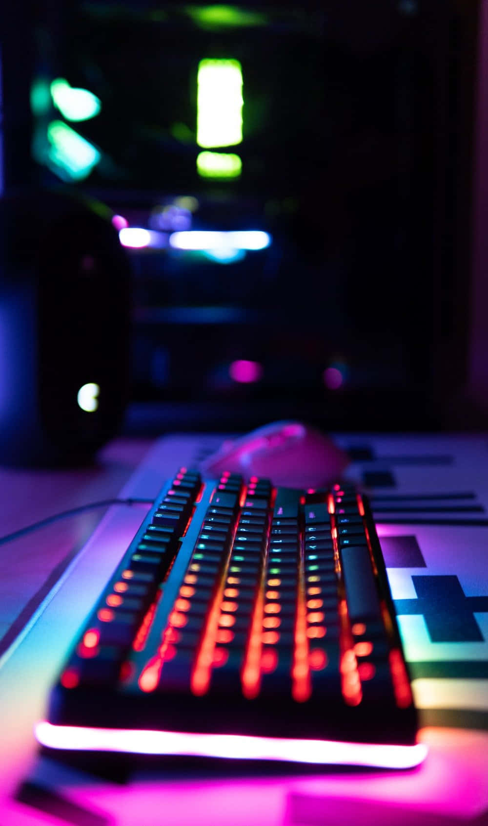 Cute Keyboard 桌布 壁紙 — 一個發光的紅色背光鍵盤和滑鼠放在一張桌子上，桌子被背景中模糊的遊戲電腦散發出的鮮豔紫色和藍色霓虹燈光所籠罩。