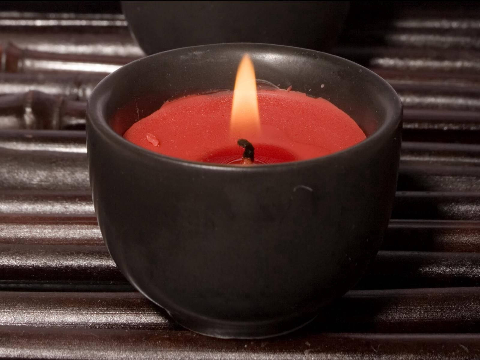 Black And Red 桌布 壁紙 — 一個發光的紅色蠟燭放在啞光黑色碗中，置於深色竹條上，在寧靜的靜物畫中投射出溫暖的光芒。