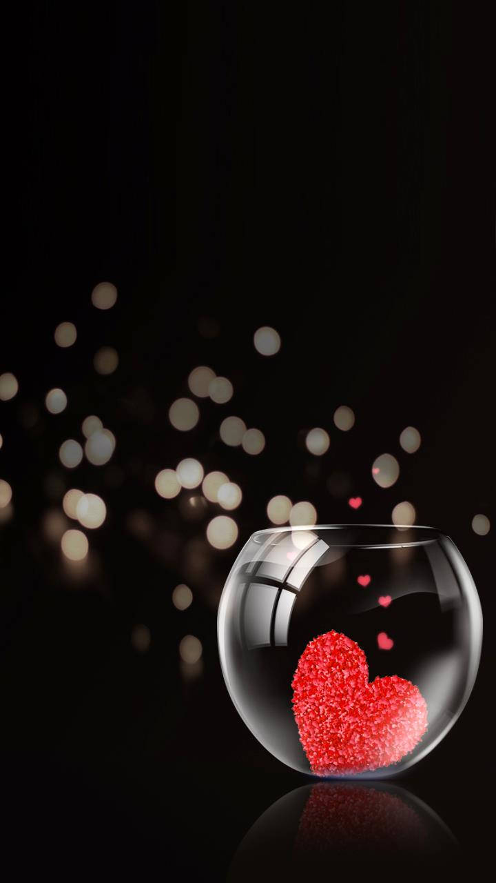 Love Phone 桌布 壁紙 — 一個發光的紅色閃粉愛心漂浮在透明玻璃魚缸中，背景是帶有柔和散景燈光的深色背景。
