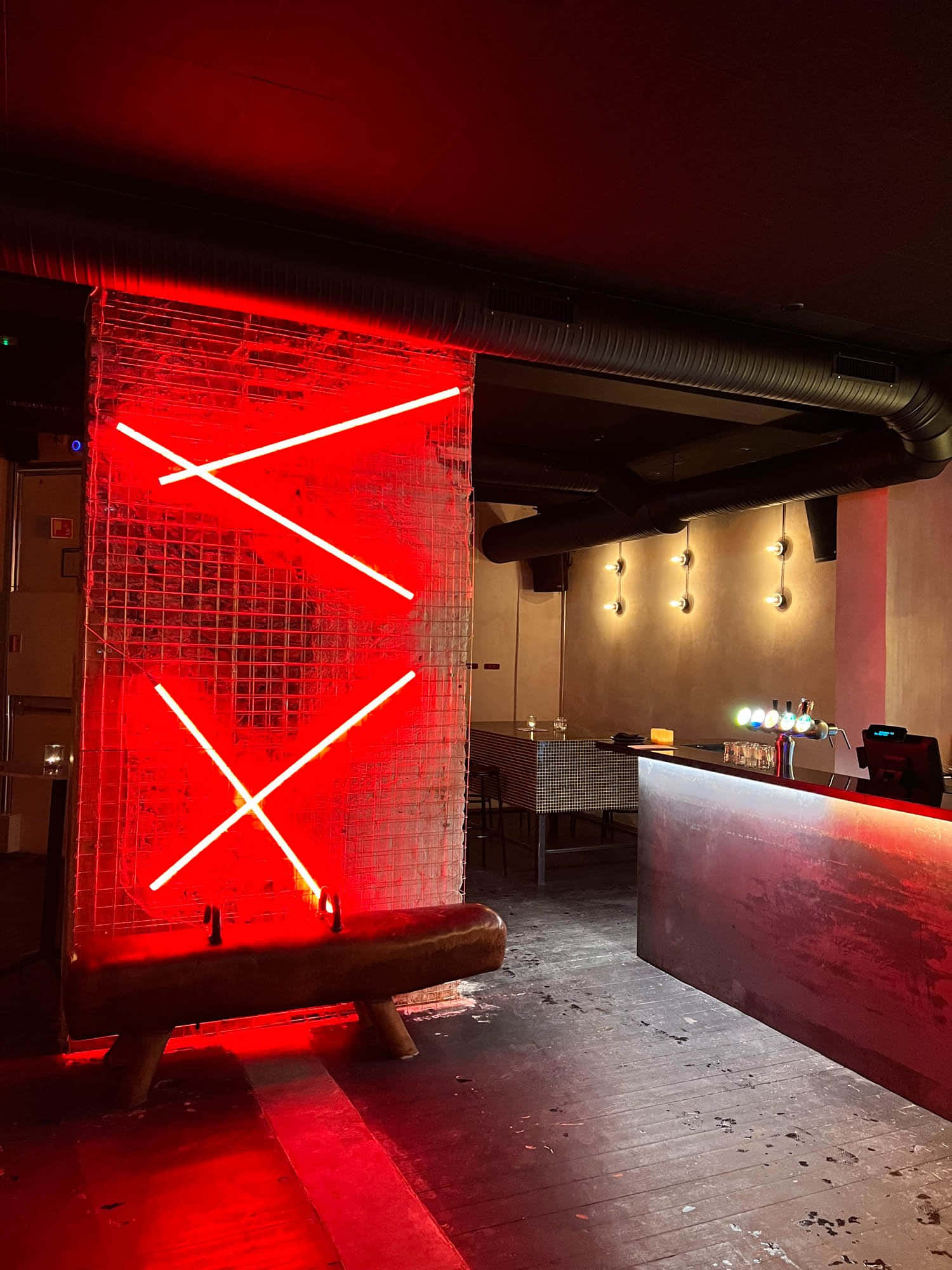 Red Room 桌布 壁紙 — 一個發光的紅色霓虹十字架雕塑照亮了昏暗的工業風格酒吧，帶有裸露的管道和木地板。
