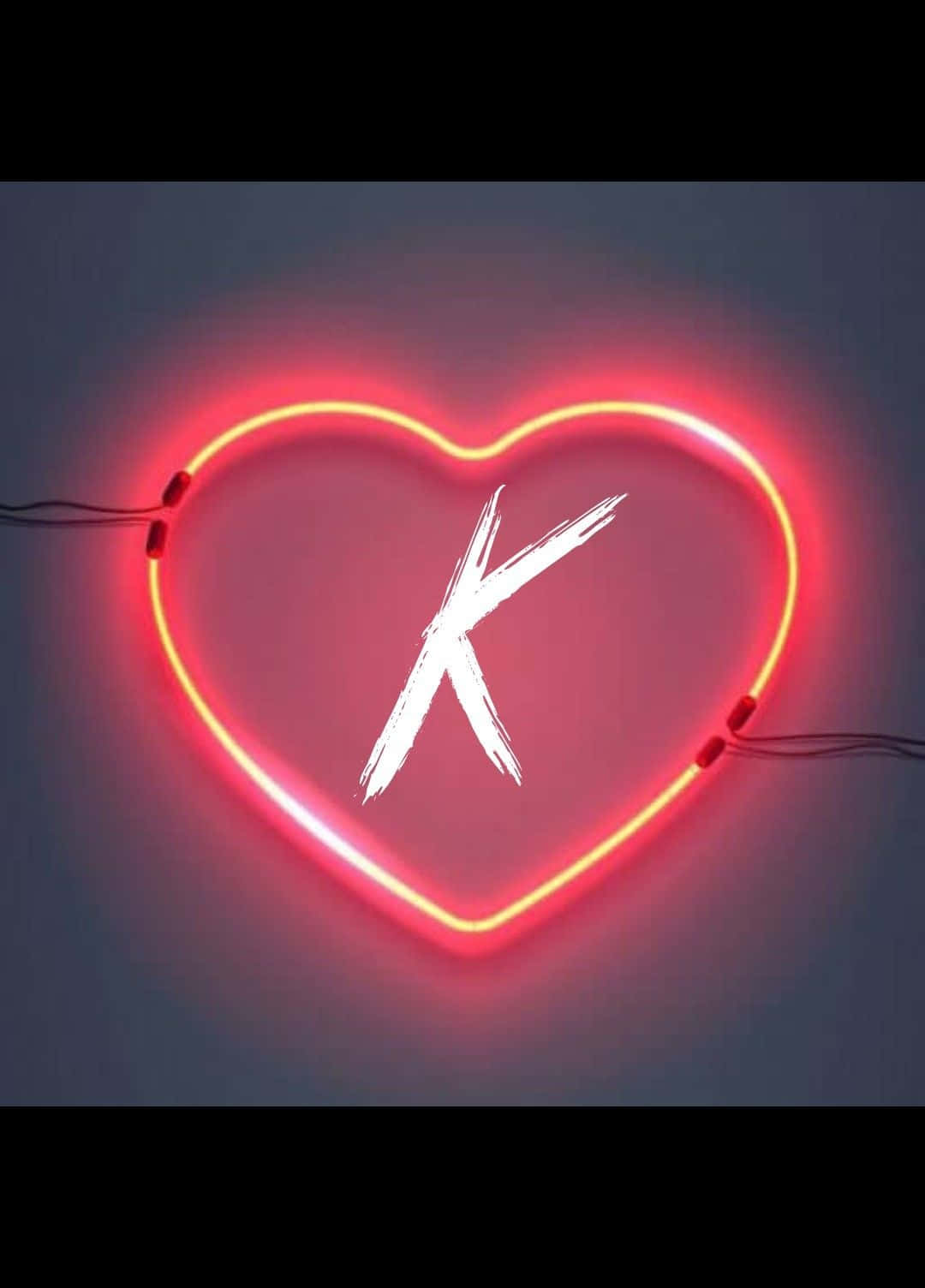 K 桌布 壁紙 — 一個發光的紅色霓虹心形，中央有一個白色筆觸字母K，安裝在深灰色牆上。