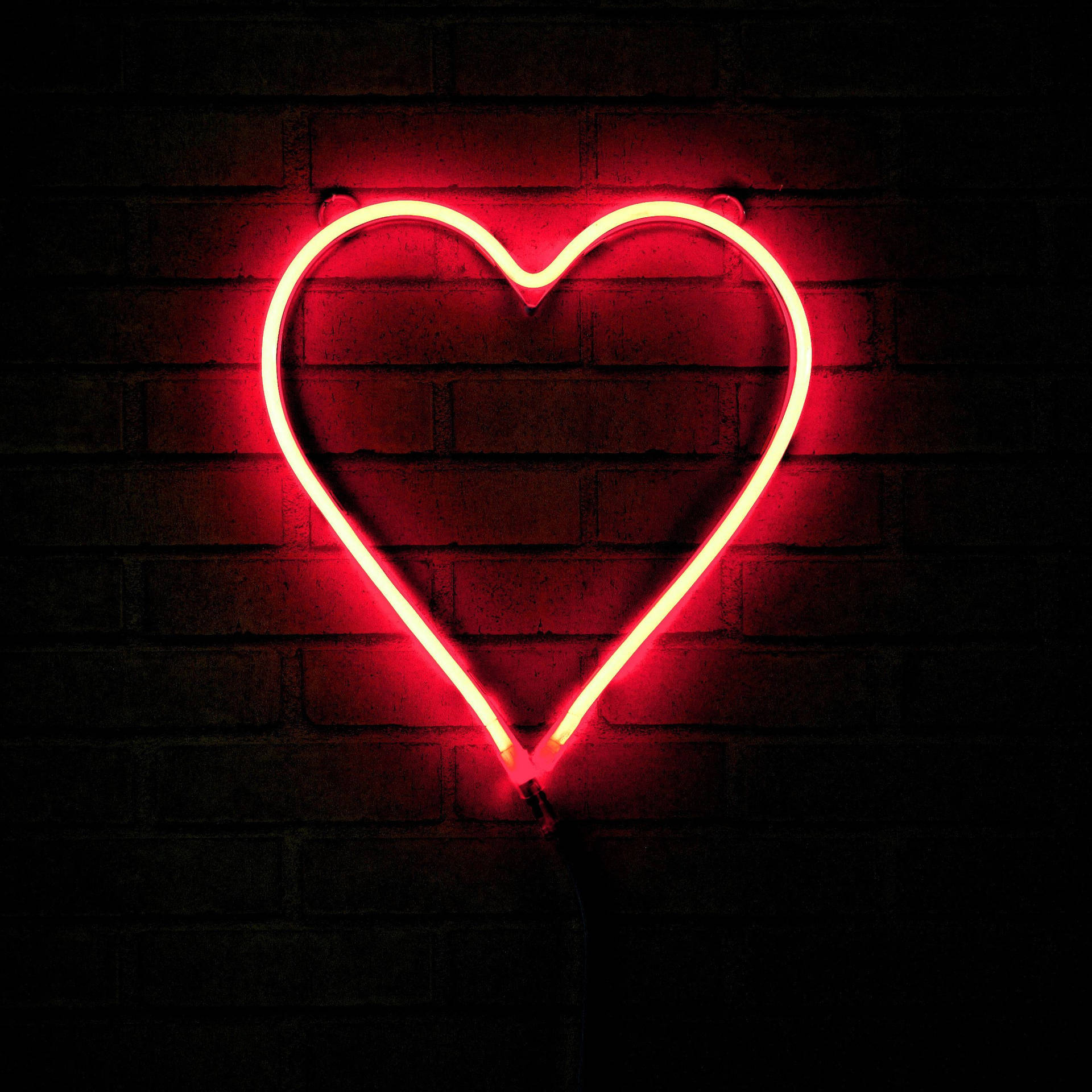 Heart 桌布 壁紙 — 一個發光的紅色霓虹心心標誌照亮了深色磚牆，溫暖的光線投射出柔和的陰影。