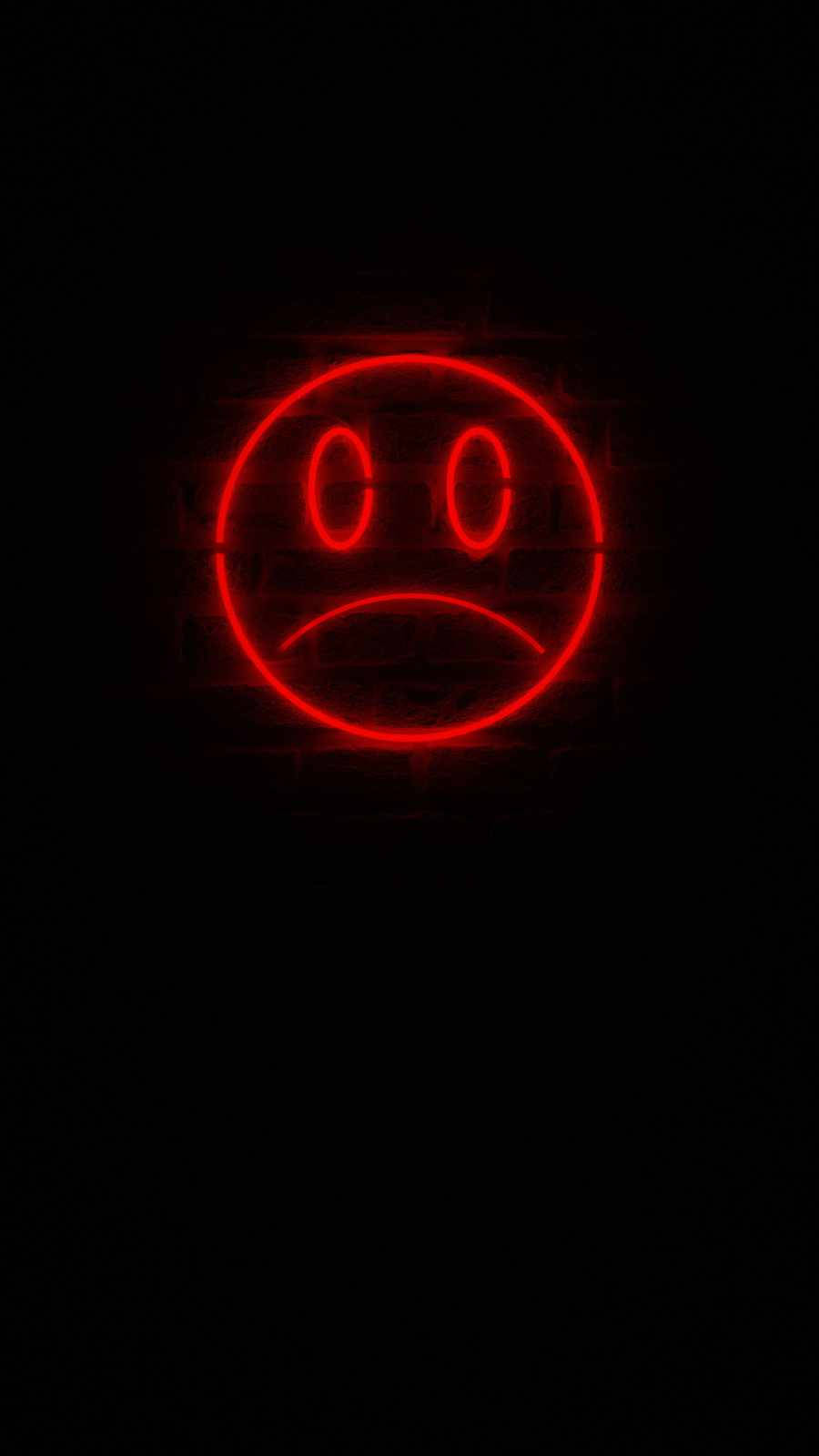 Sad Emoji 桌布 壁紙 — 一個發光的紅色霓虹悲傷符號在黑暗的磚牆上投射出昏暗的光線，營造出憂鬱的城市氛圍。