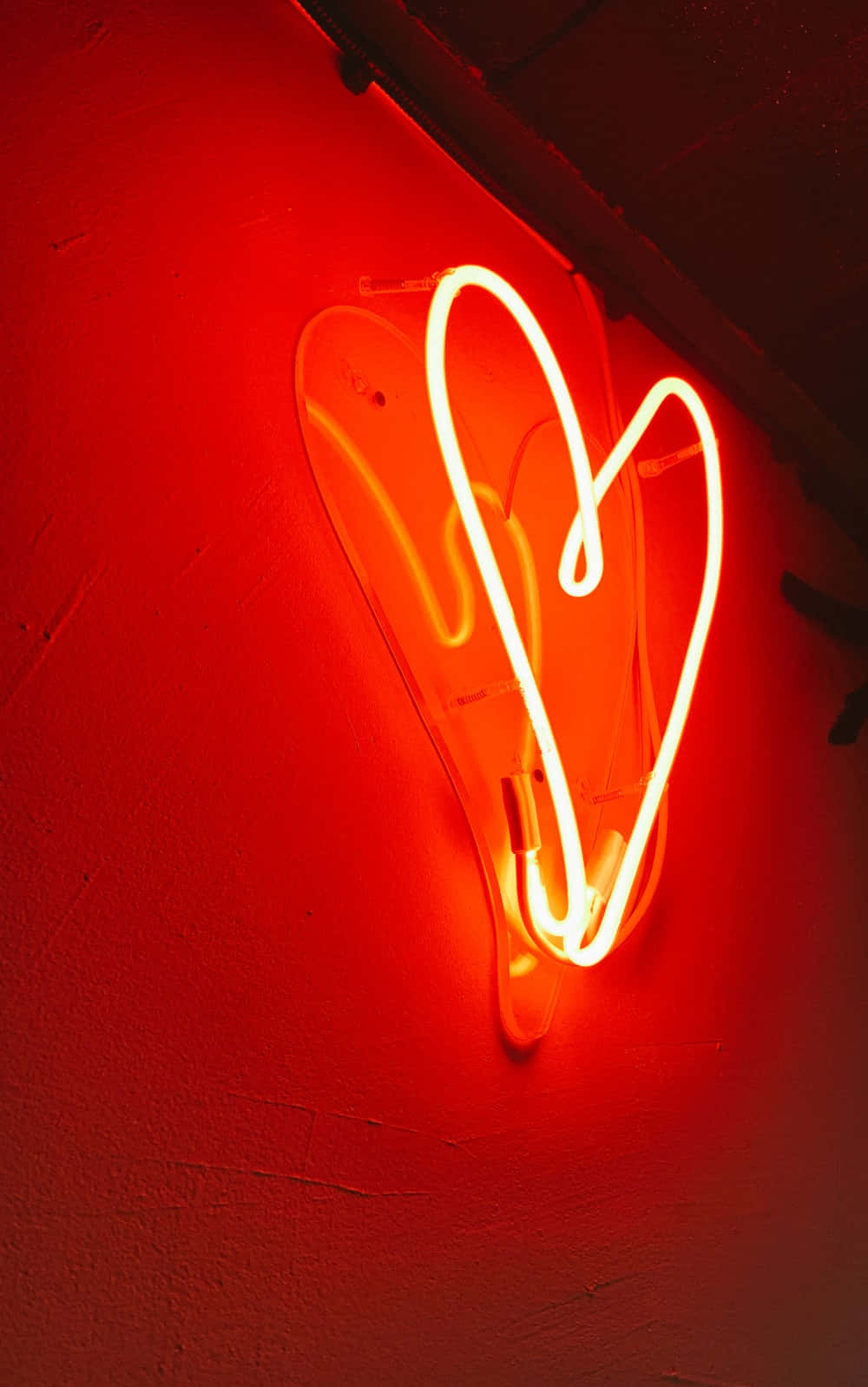 Orange Heart 桌布 壁紙 — 一個發光的紅色霓虹愛心在昏暗的空間中，在帶有紋理的牆壁上投射出溫暖的光芒。