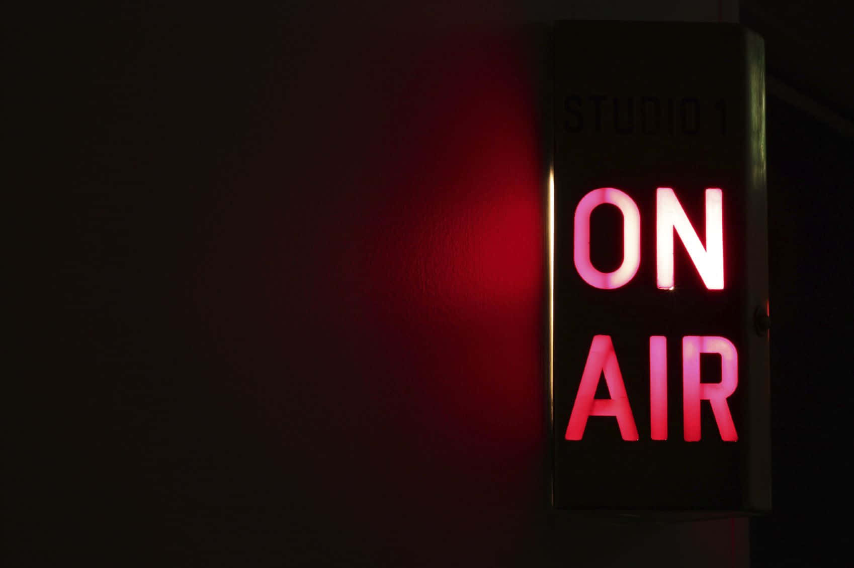 Broadcast 桌布 壁紙 — 一個發光的紅色霓虹燈「ON AIR」標誌在廣播工作室的暗牆上投射出溫暖的光芒。
