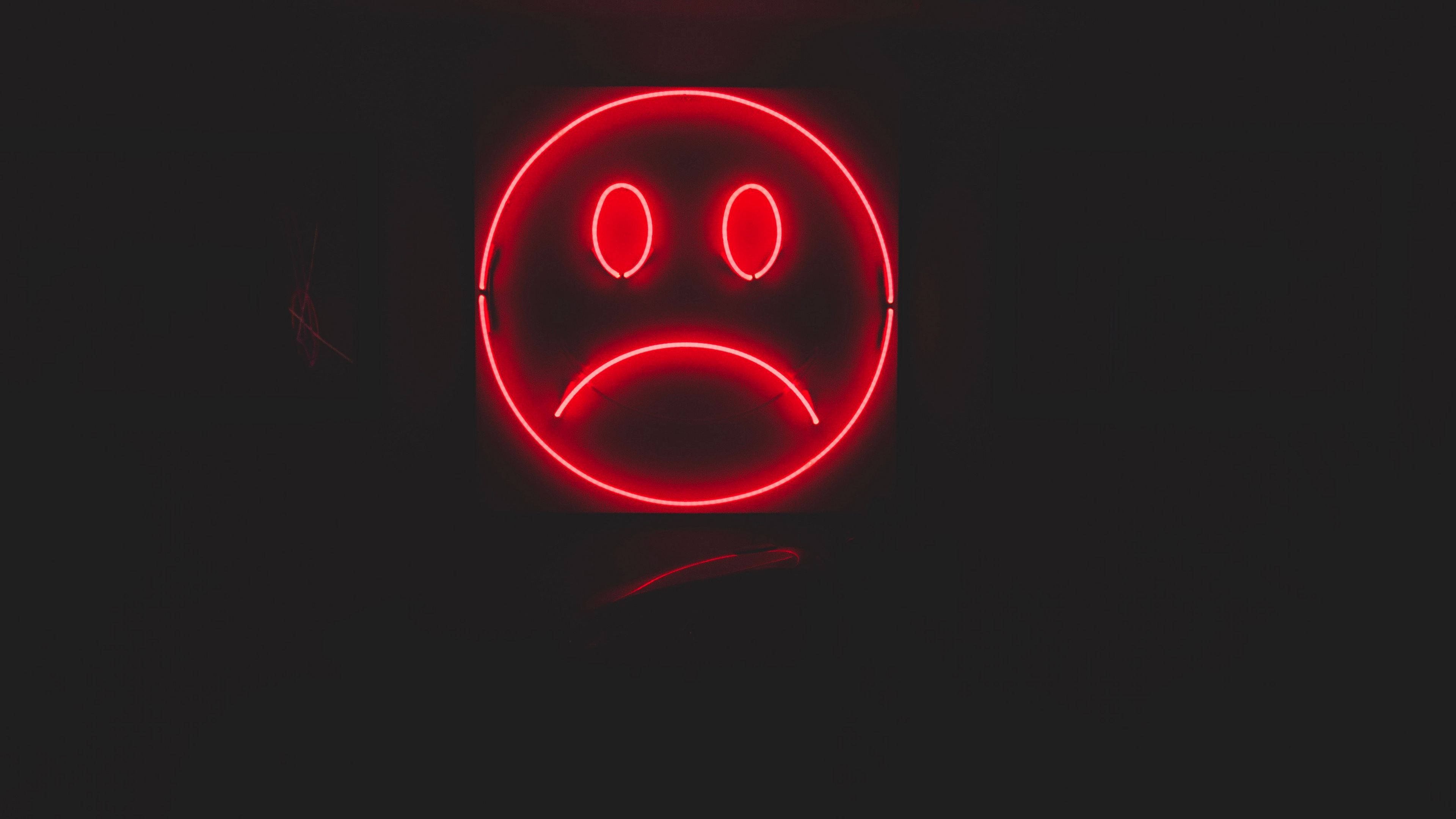 Sad Emoji 桌布 壁紙 — 一個發光的紅色霓虹燈悲傷臉標誌在漆黑背景中閃耀。